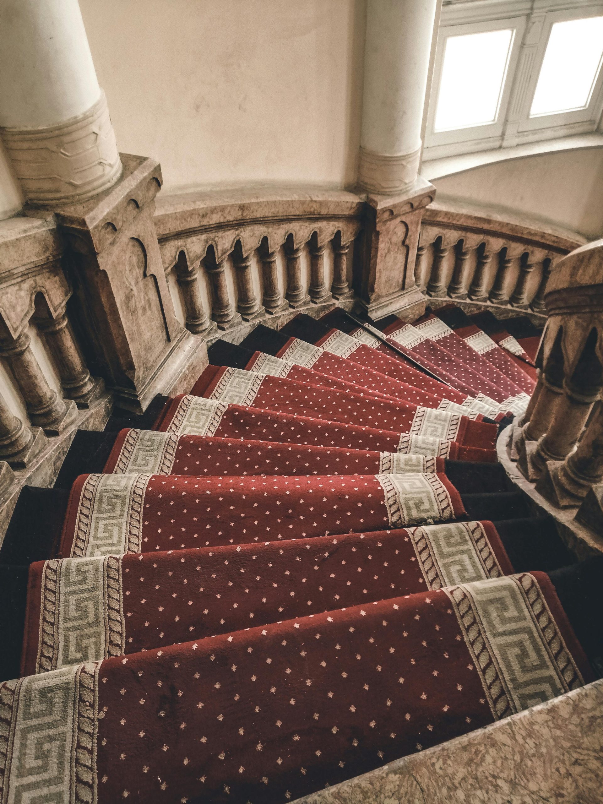 A beautifully crafted spiral staircase adorned with a red carpet and classic pillar design.