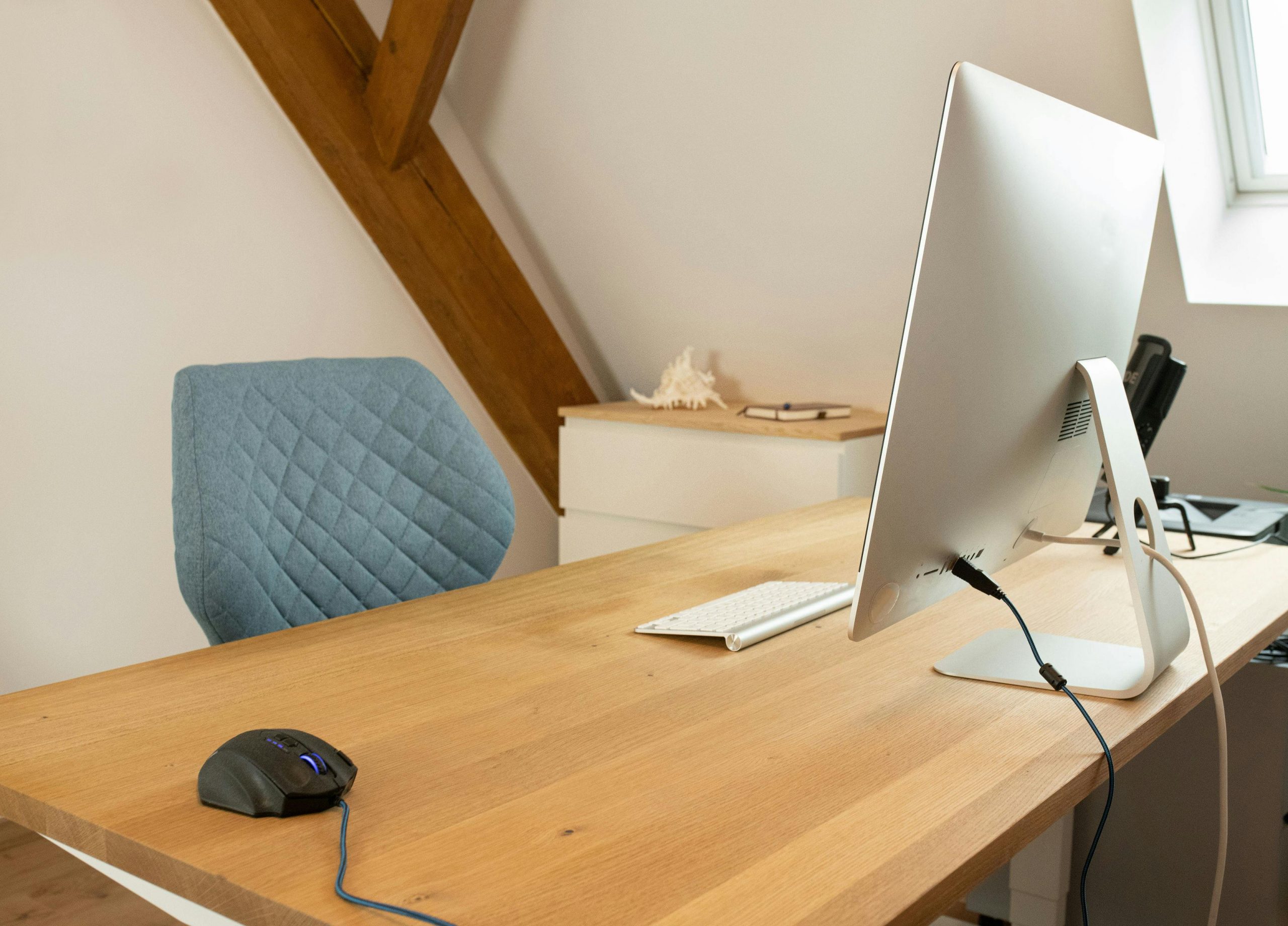 A minimalist home office setup featuring a wooden desk, computer monitor, and ergonomic chair.