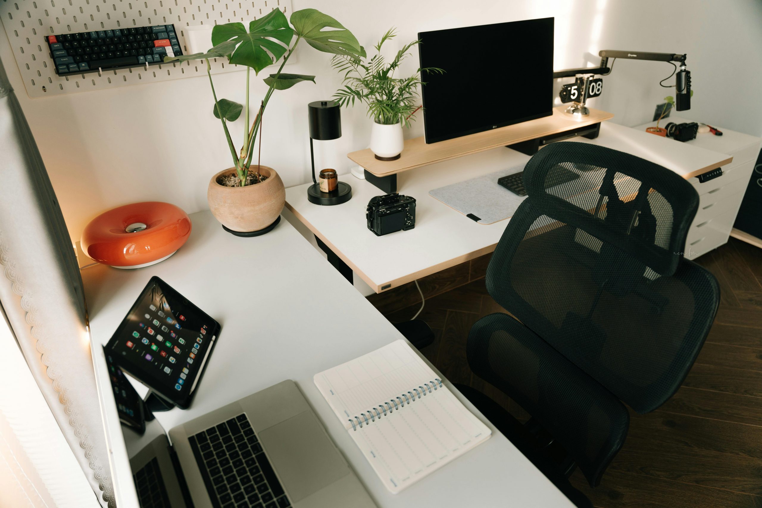 A stylish home office setup featuring tech gadgets, a monitor, a tablet, and decorative plants in a minimalist design.
