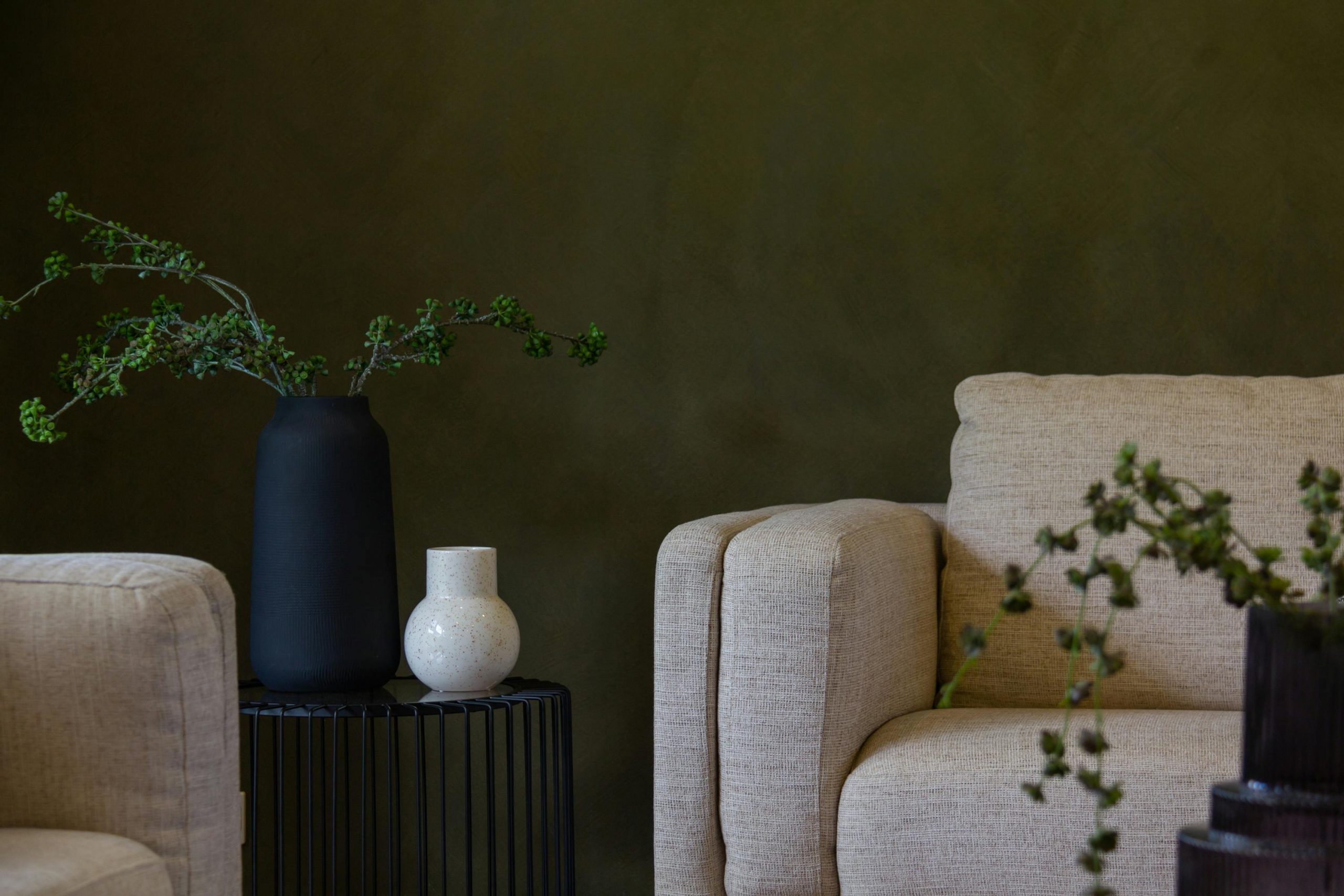 A stylish, minimalist living room with modern furniture and decor, featuring green walls and neutral tones.