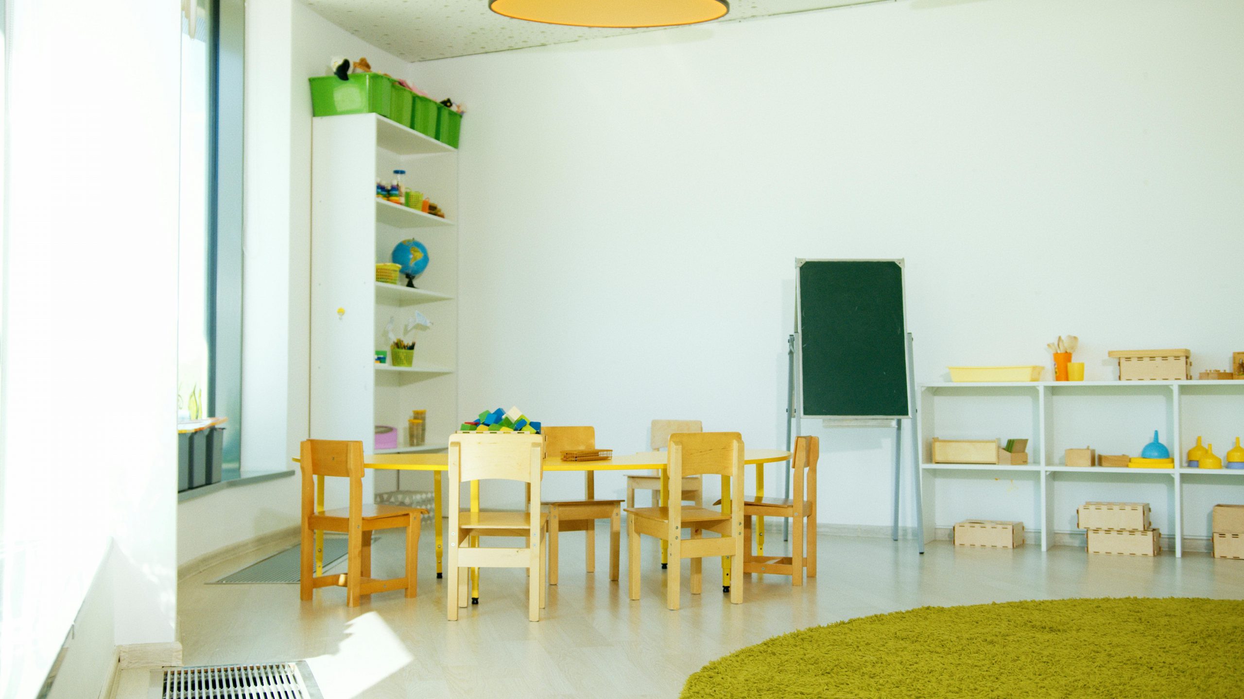 A well-lit, colorful kindergarten classroom with chairs, tables, and educational materials.