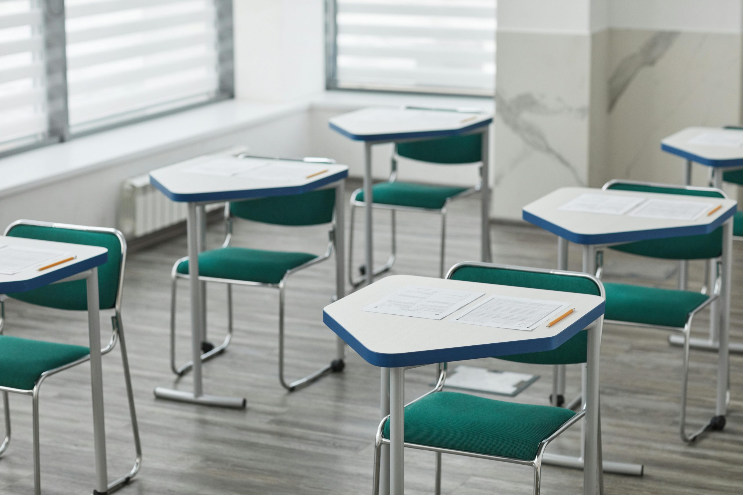 An empty classroom with arranged desks, exam papers, and pencils ready for students.