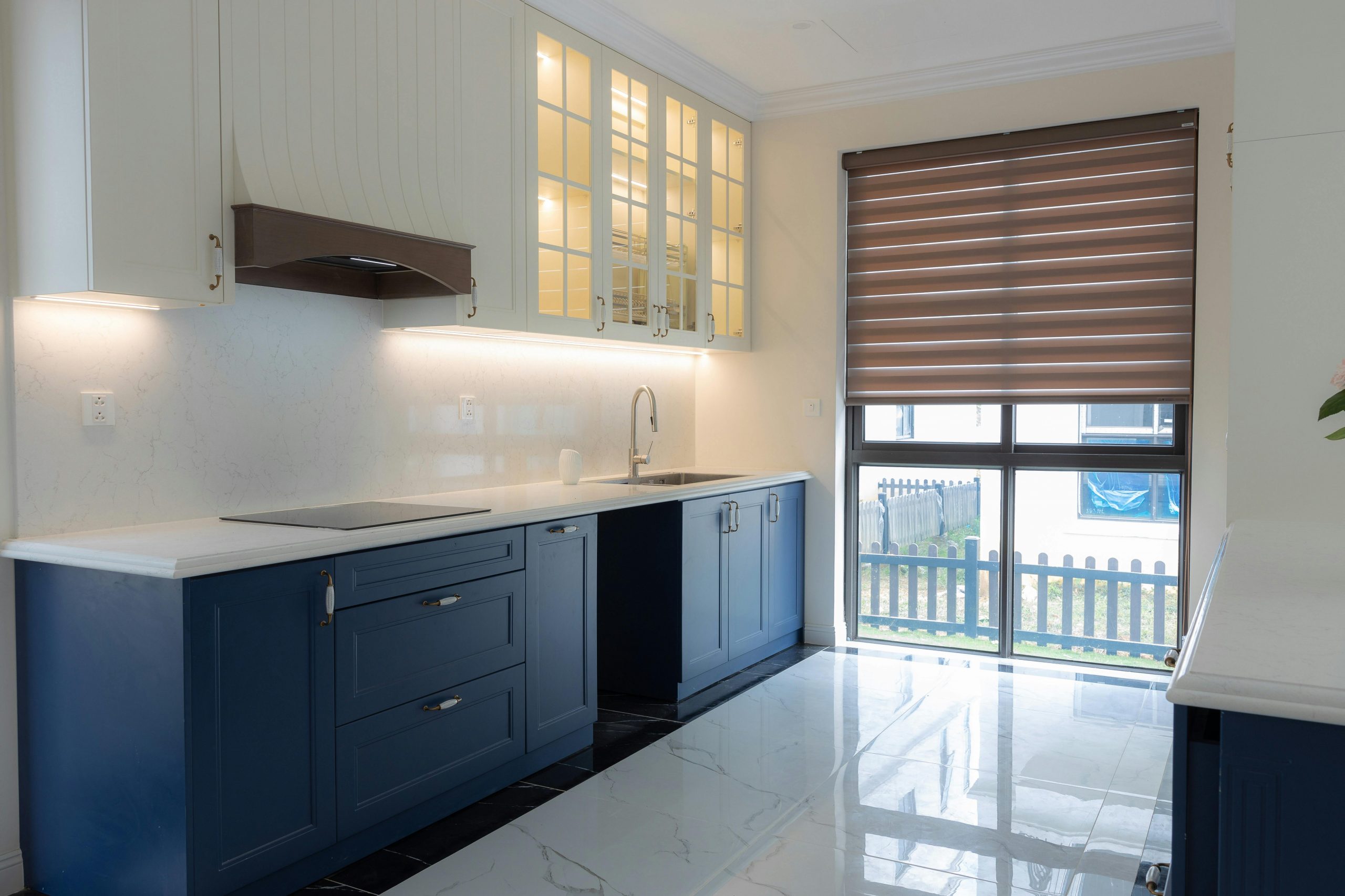 Bright modern kitchen featuring blue cabinetry, marble countertops, and ample natural light through large windows.