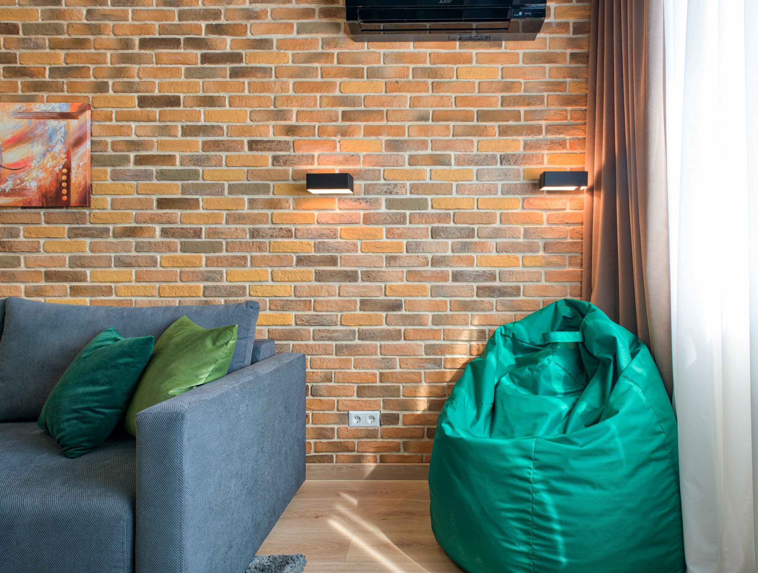 Contemporary interior featuring a brick wall, gray couch, and green bean bag chair.