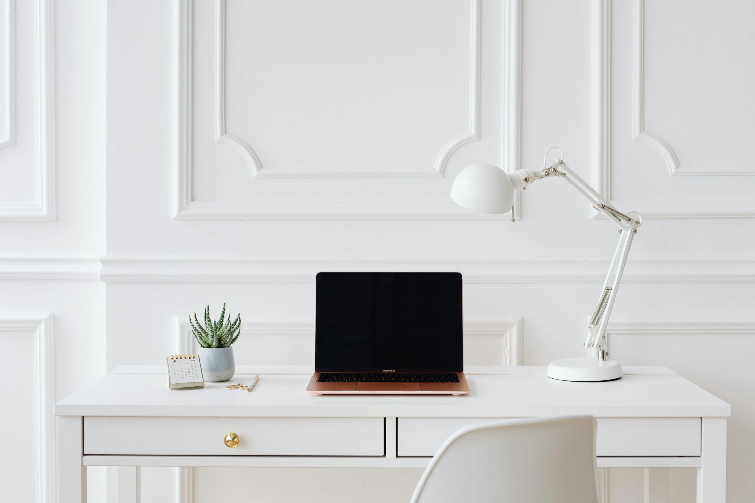 Elegant minimalist desk setup with laptop and white lamp in a bright room.