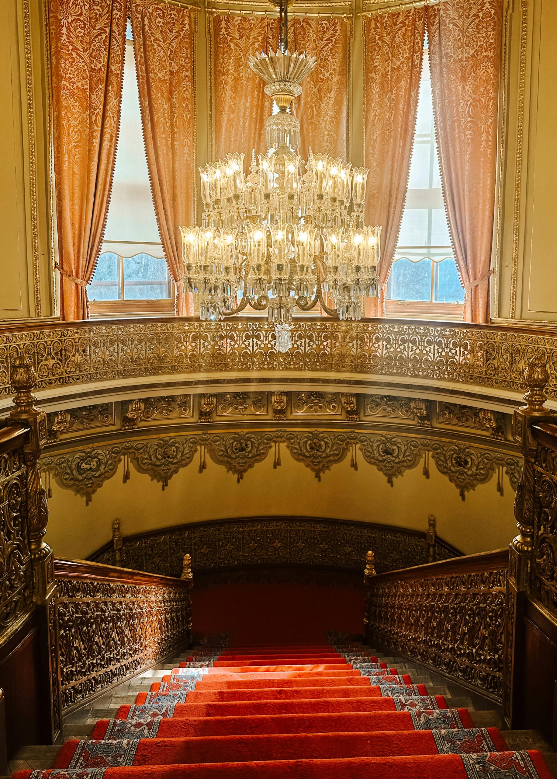 Elegant vintage staircase with ornate details and a sparkling chandelier in a historic building.