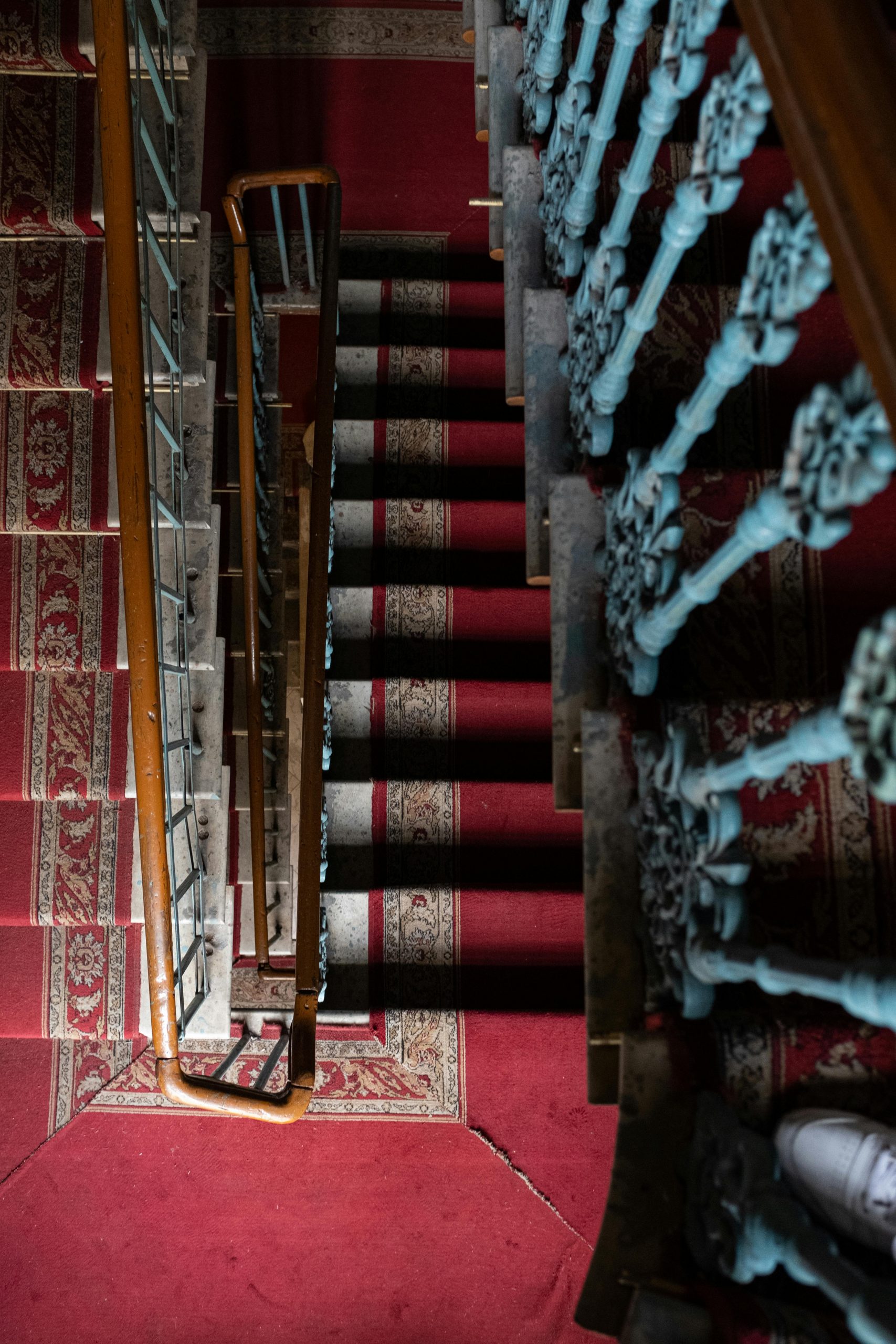 Elegant vintage staircase with ornate iron banister and red carpet in a classic interior.