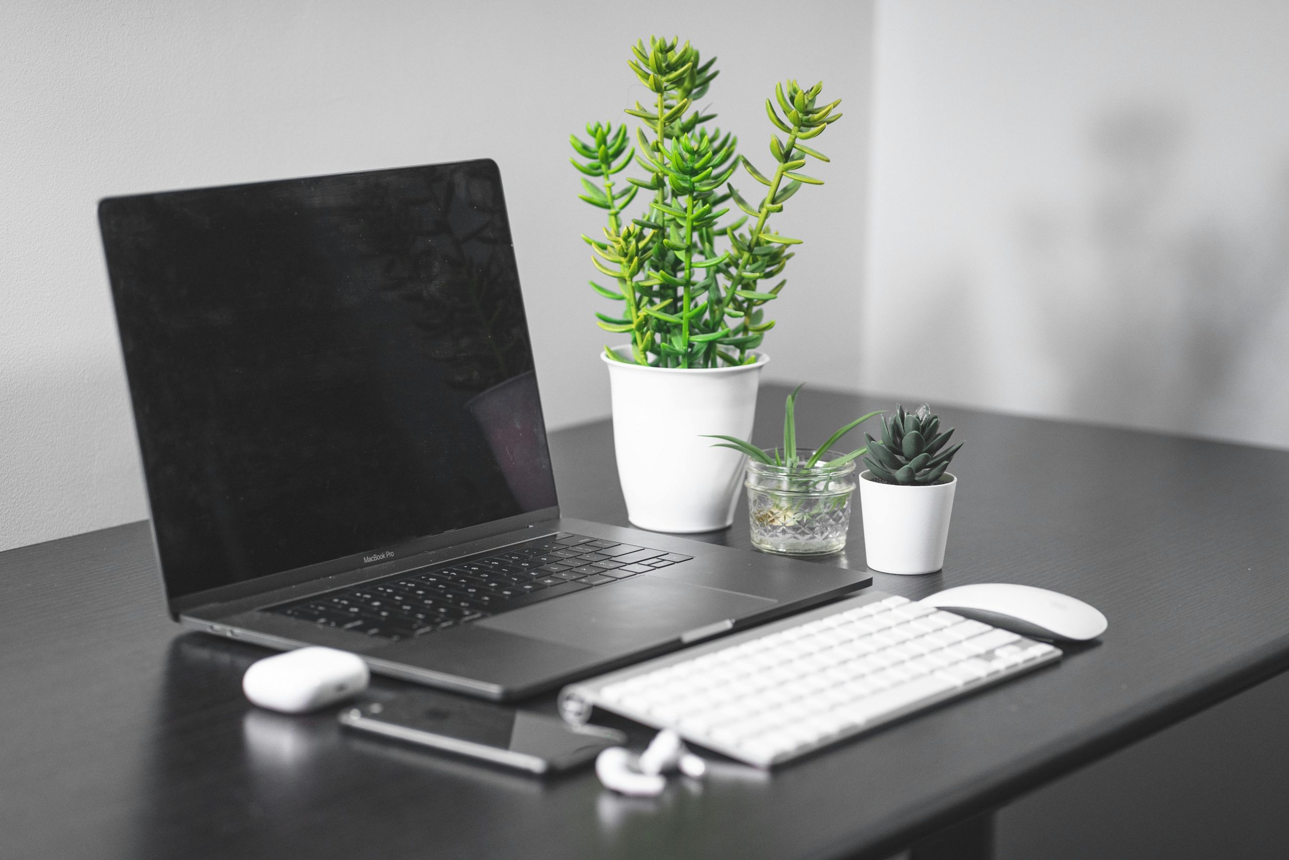 Elegant workspace featuring a MacBook, white keyboard, wireless mouse, and green plants on a minimalist black desk.