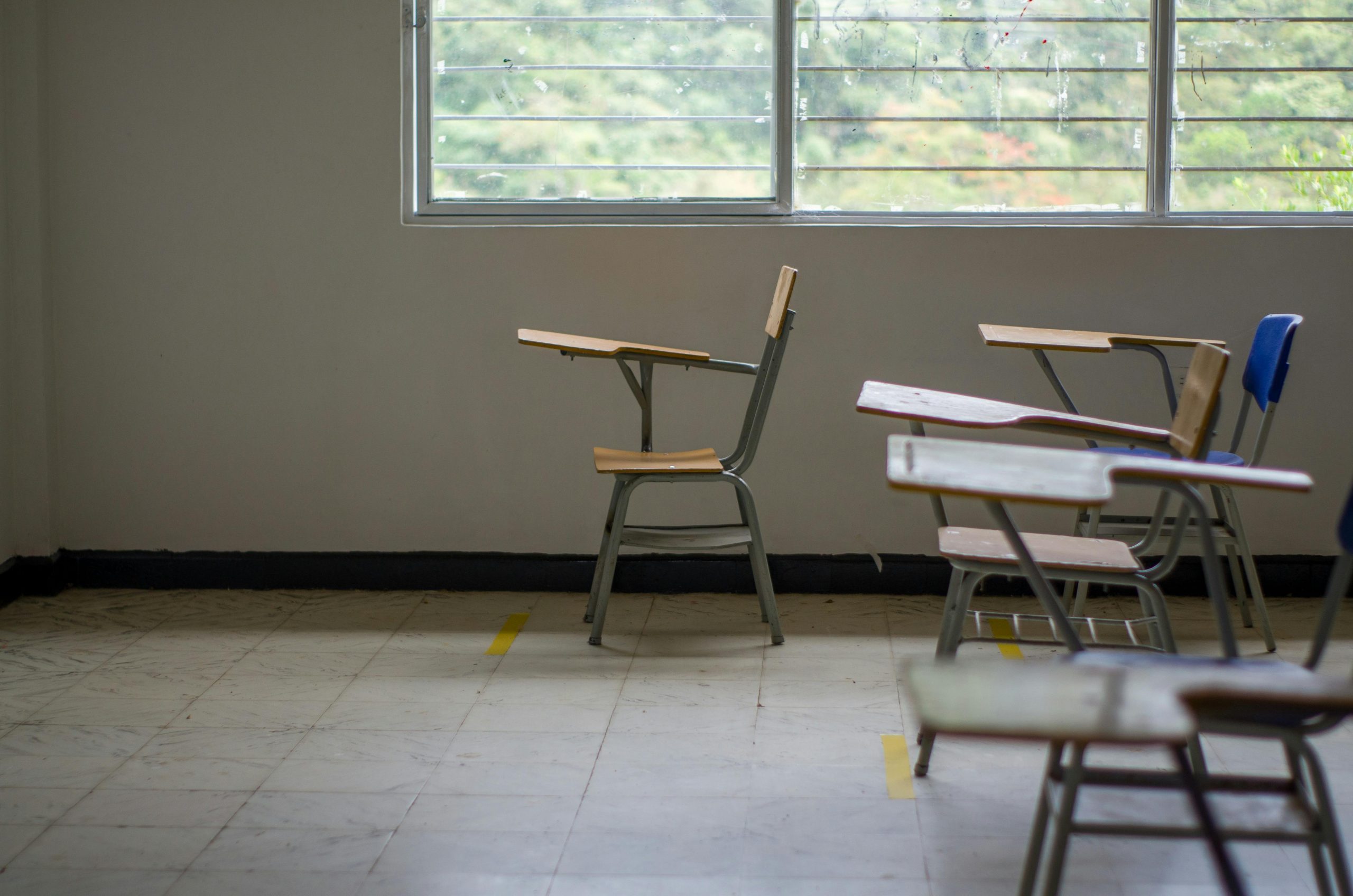 Quiet empty classroom interior with school desks by a large window.