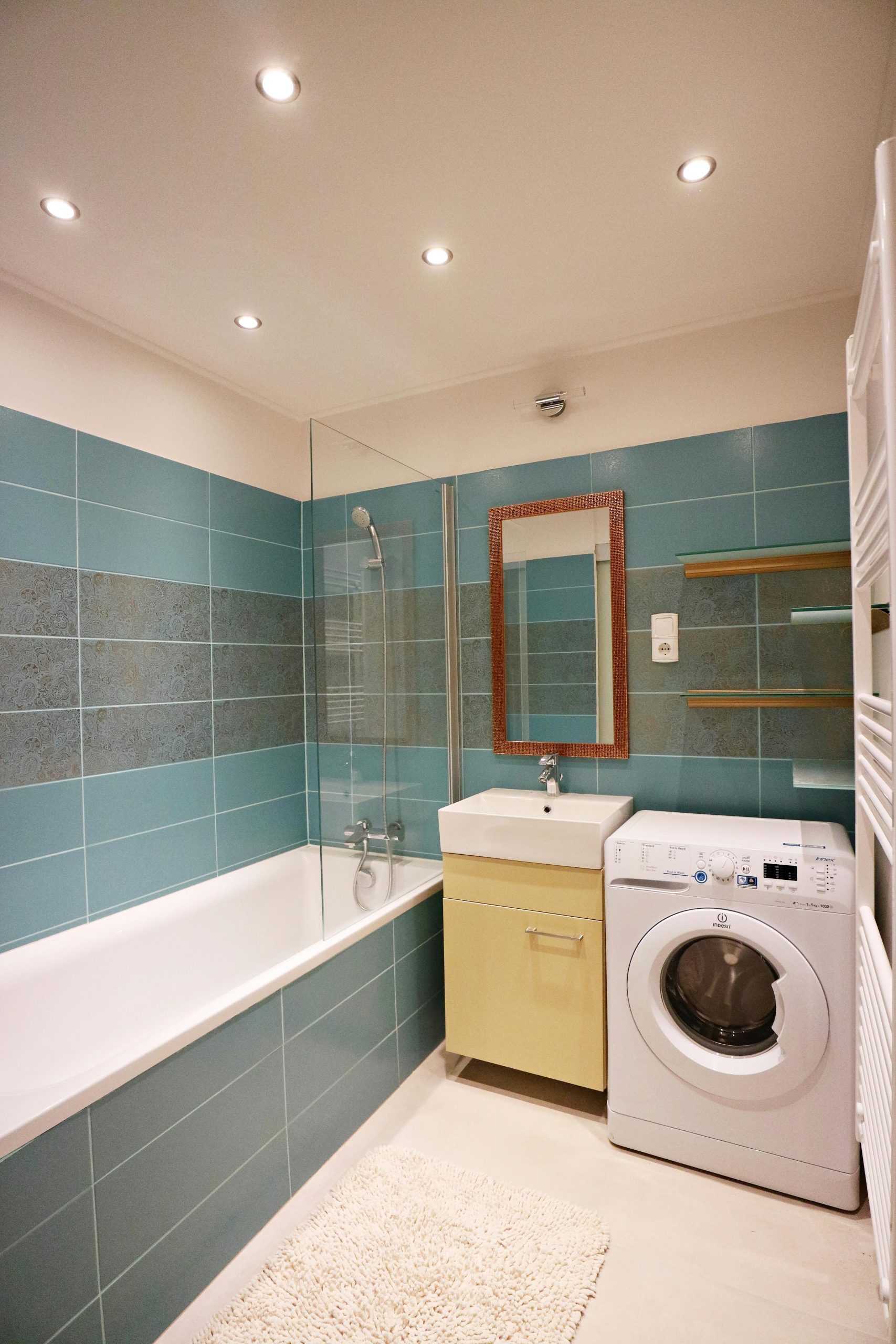 Stylish bathroom featuring green tiles, bathtub, and washing machine.