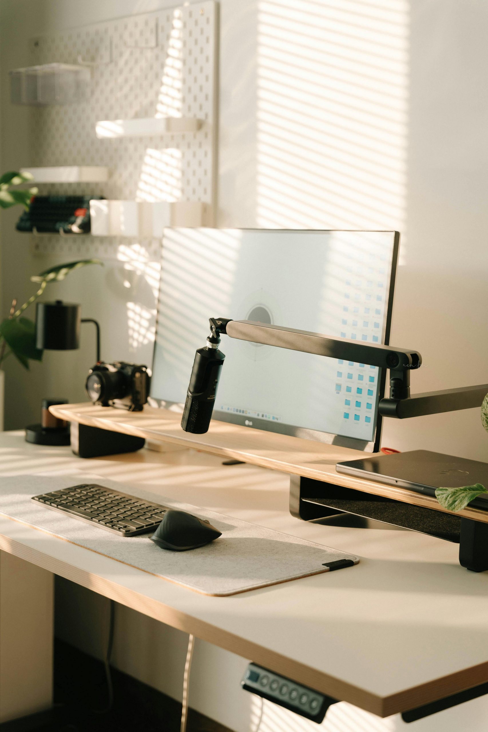 Sunlit home office setup with computer, keyboard, and microphone, embodying minimalism and modern design.