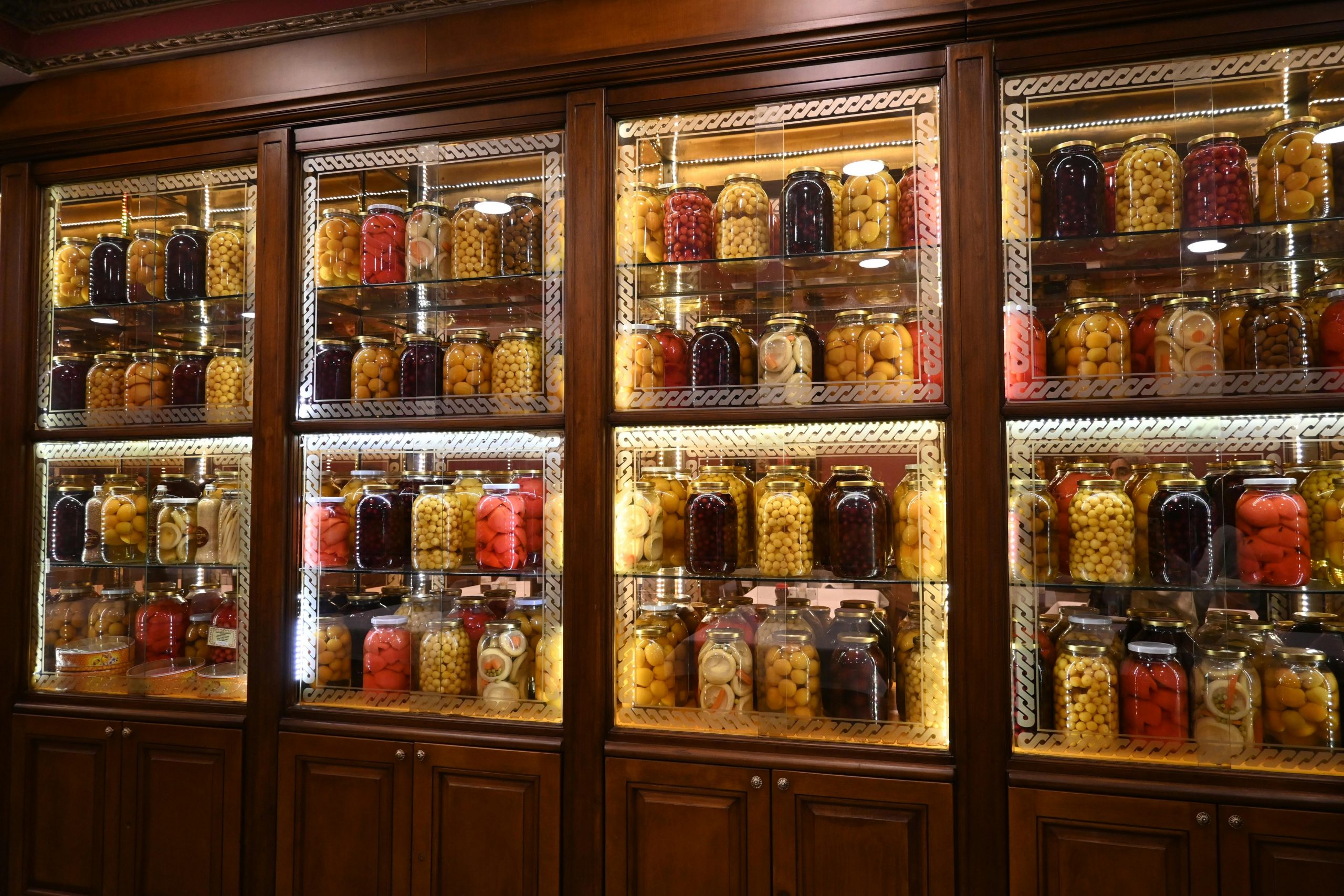 Vibrant shelves of preserved fruits and vegetables in glass jars on a wooden cabinet in Istanbul, Türkiye.