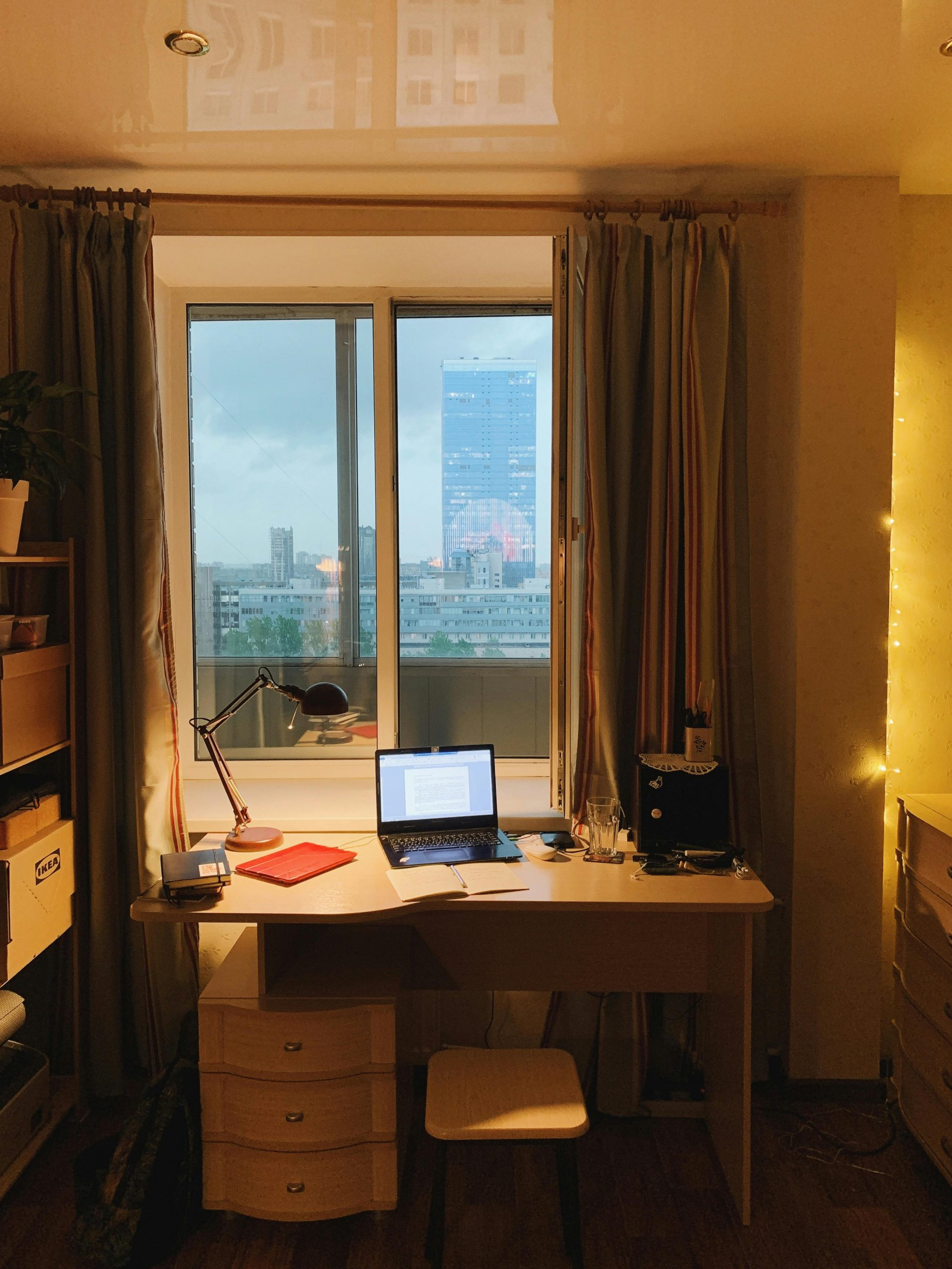 Warm evening scene of a home office with a view of Sankt-Peterburg's urban skyline through the window.