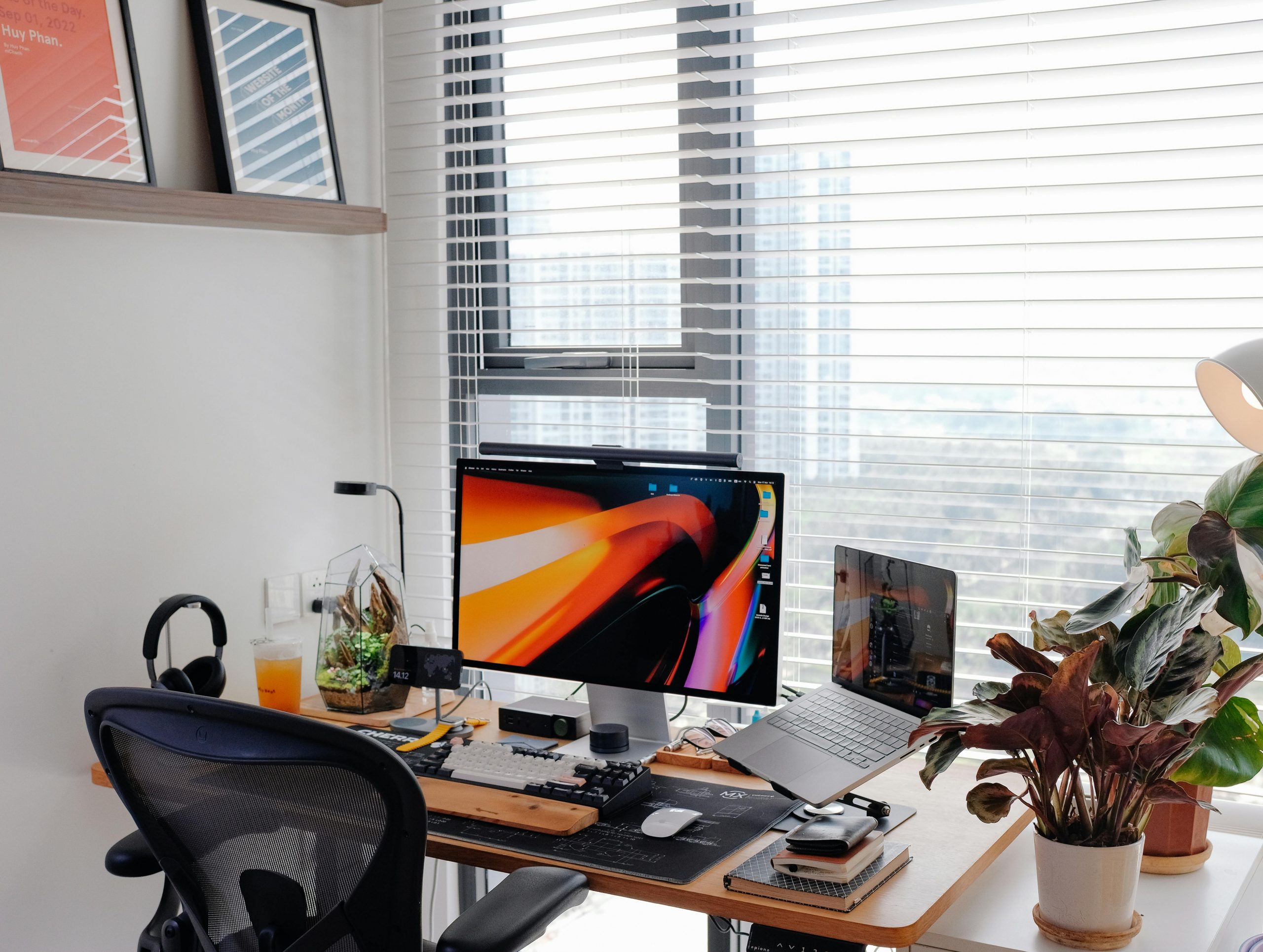 Well-organized home office with tech gadgets and plants by a window overlooking nature.