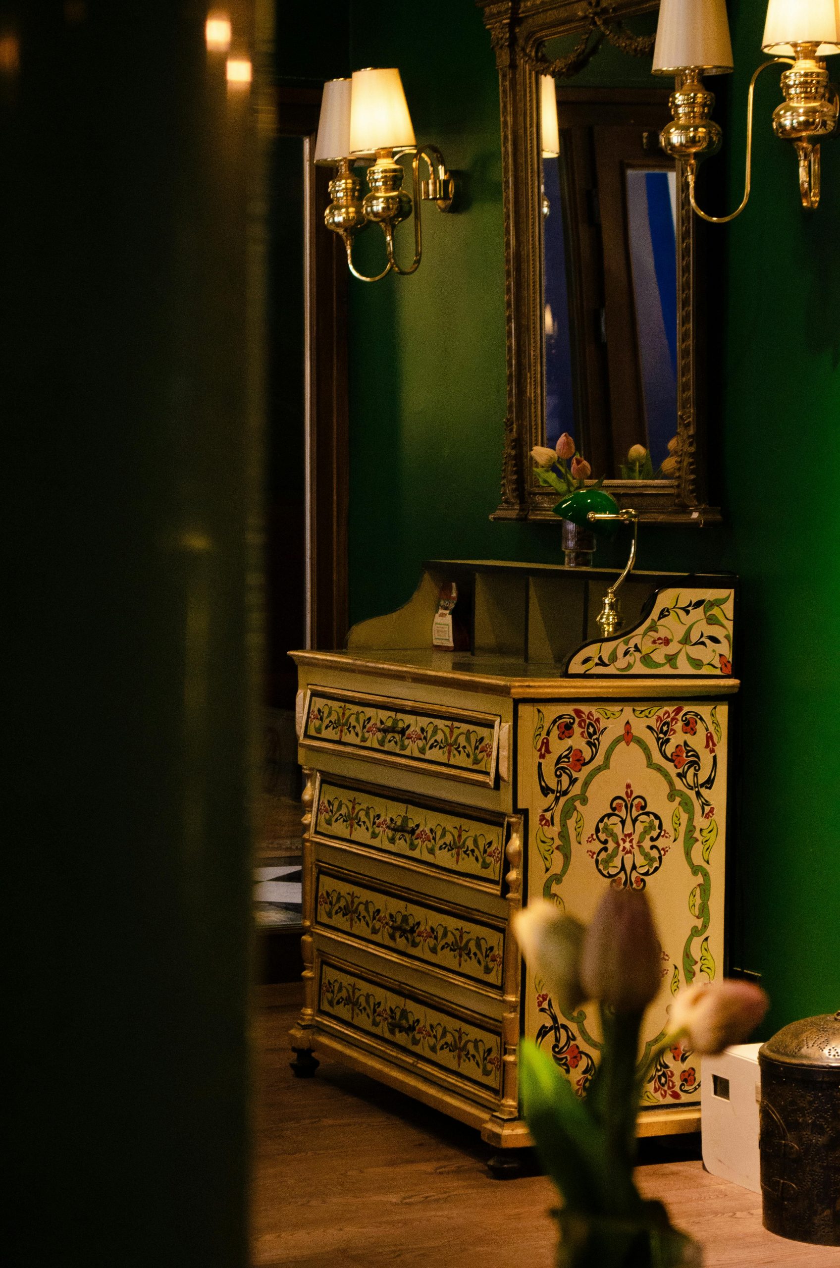 A charming vintage room showcasing an antique mirror, floral dresser, and warm lighting.