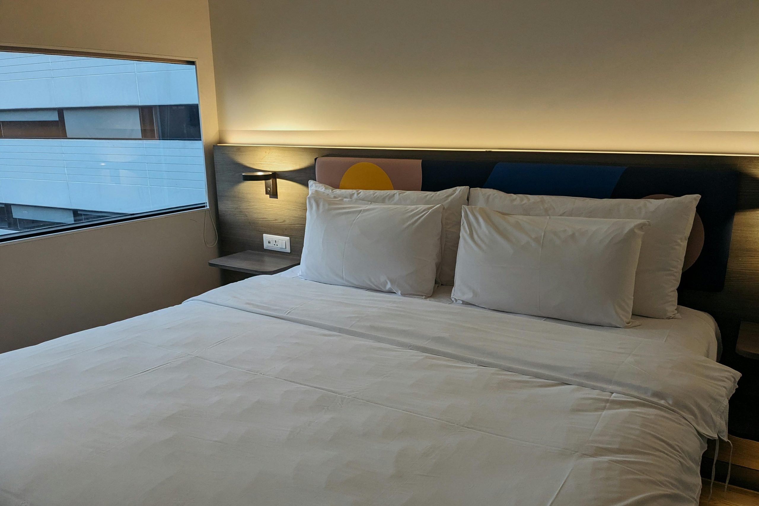 A cozy and modern hotel room featuring a neatly made bed with white linens and a view from the window.