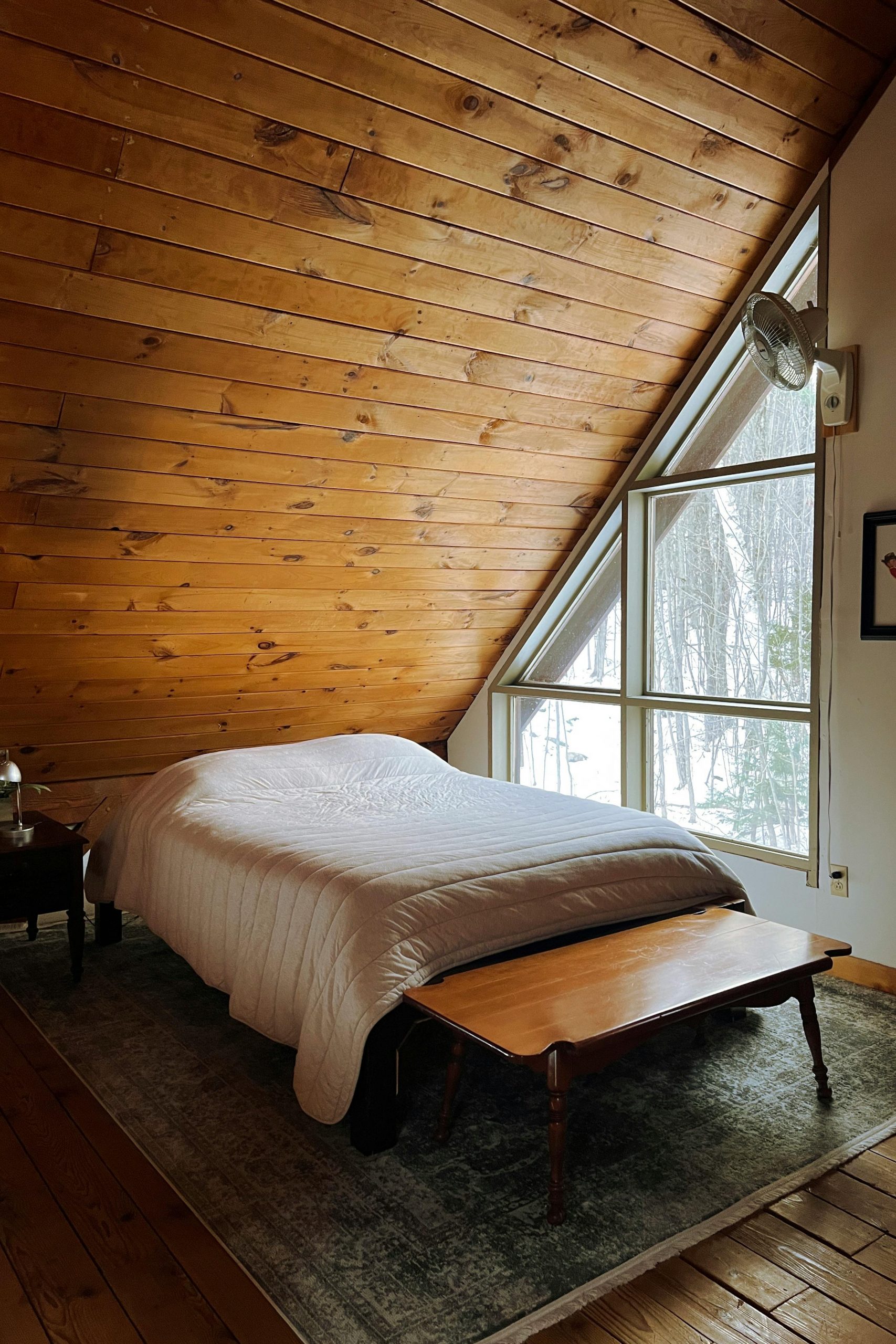 A cozy attic bedroom with wooden walls and a large window overlooking a snowy landscape.
