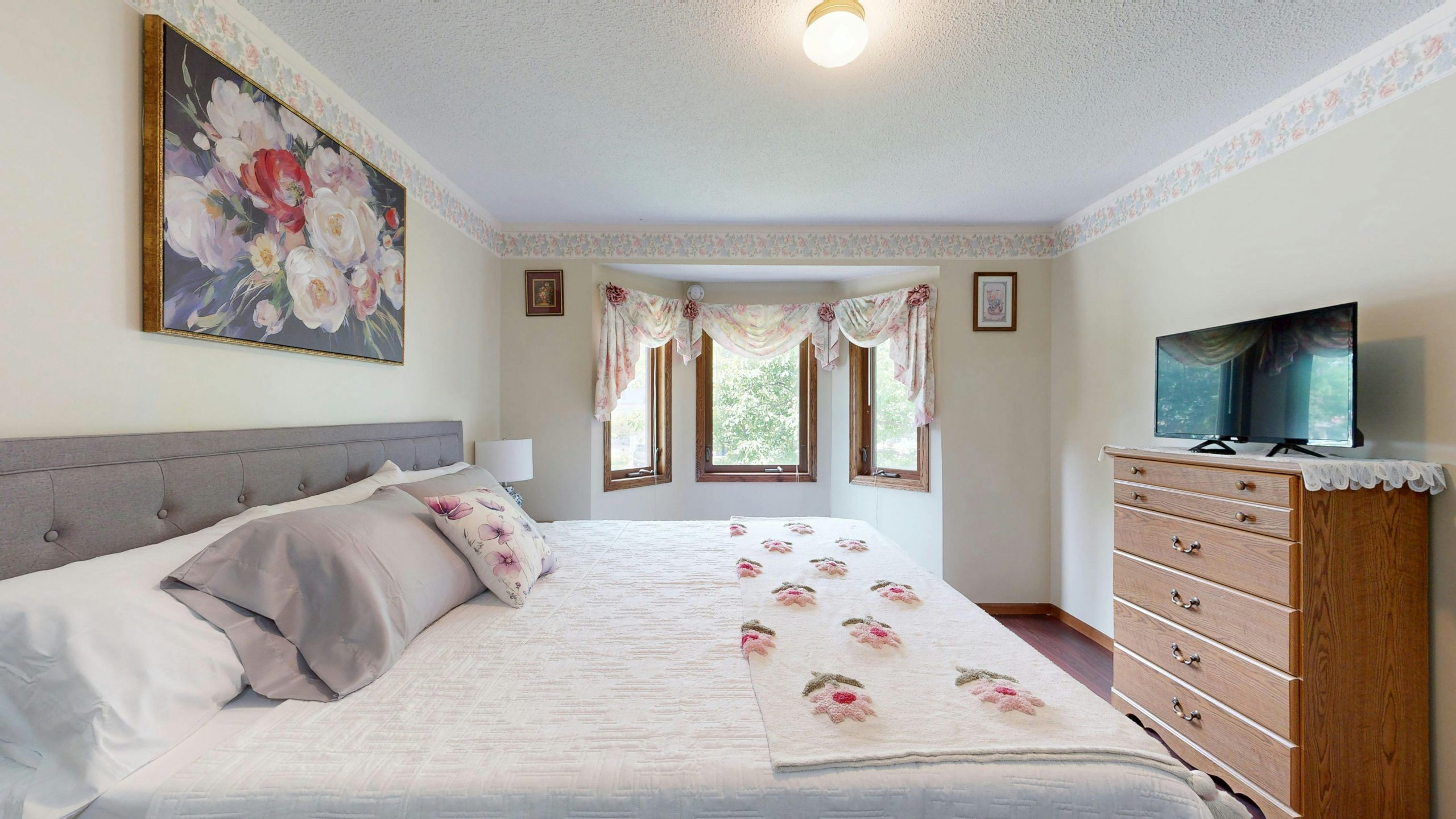 A cozy bedroom featuring floral decor and abundant natural light from bay windows.