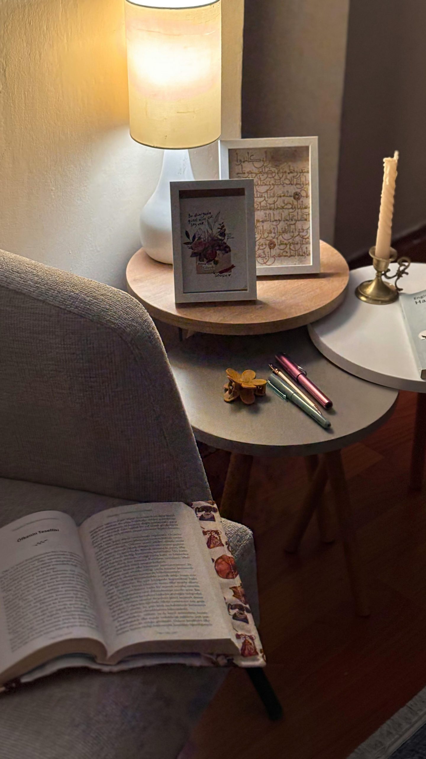 A cozy indoor reading nook featuring an open book, lamp, and decorative items on a table.