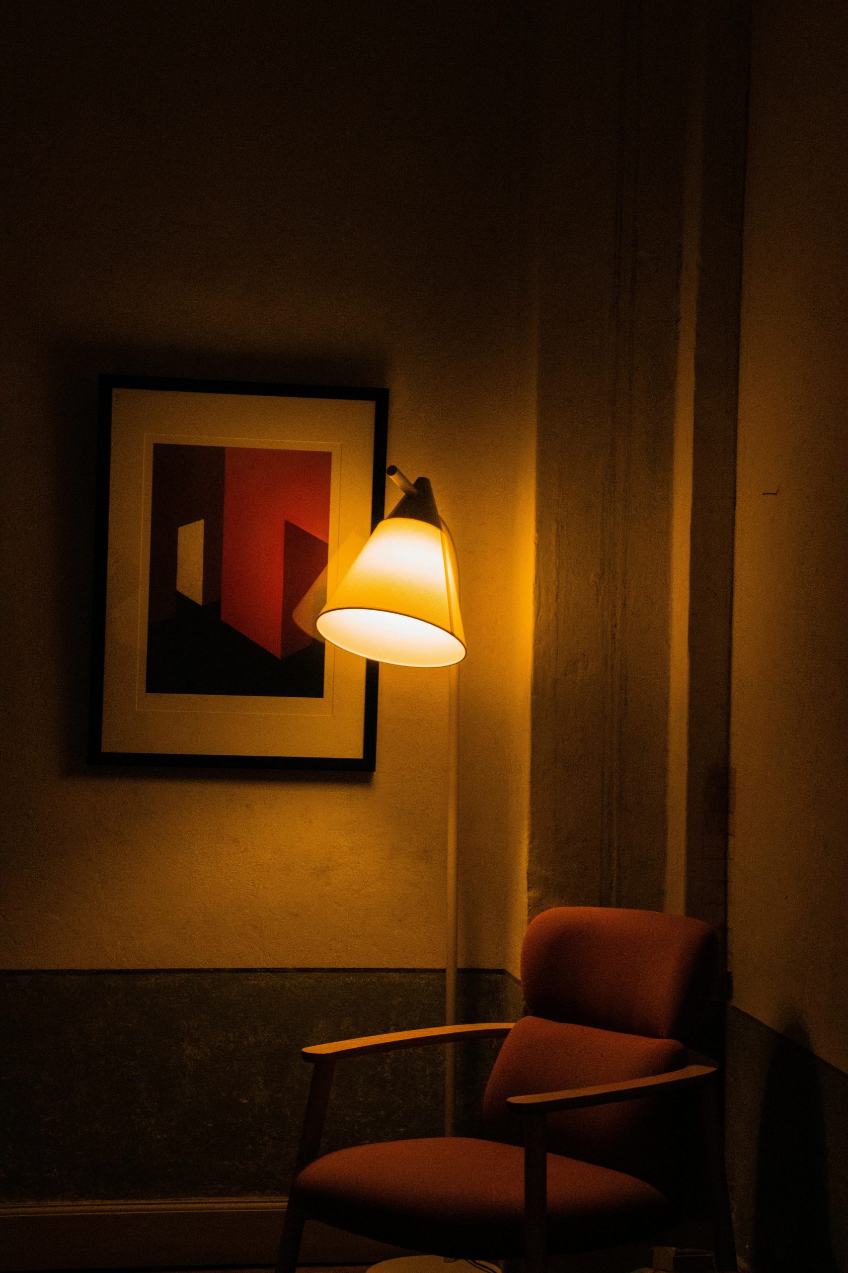 A cozy interior corner with an armchair under warm lamp light beside abstract artwork.
