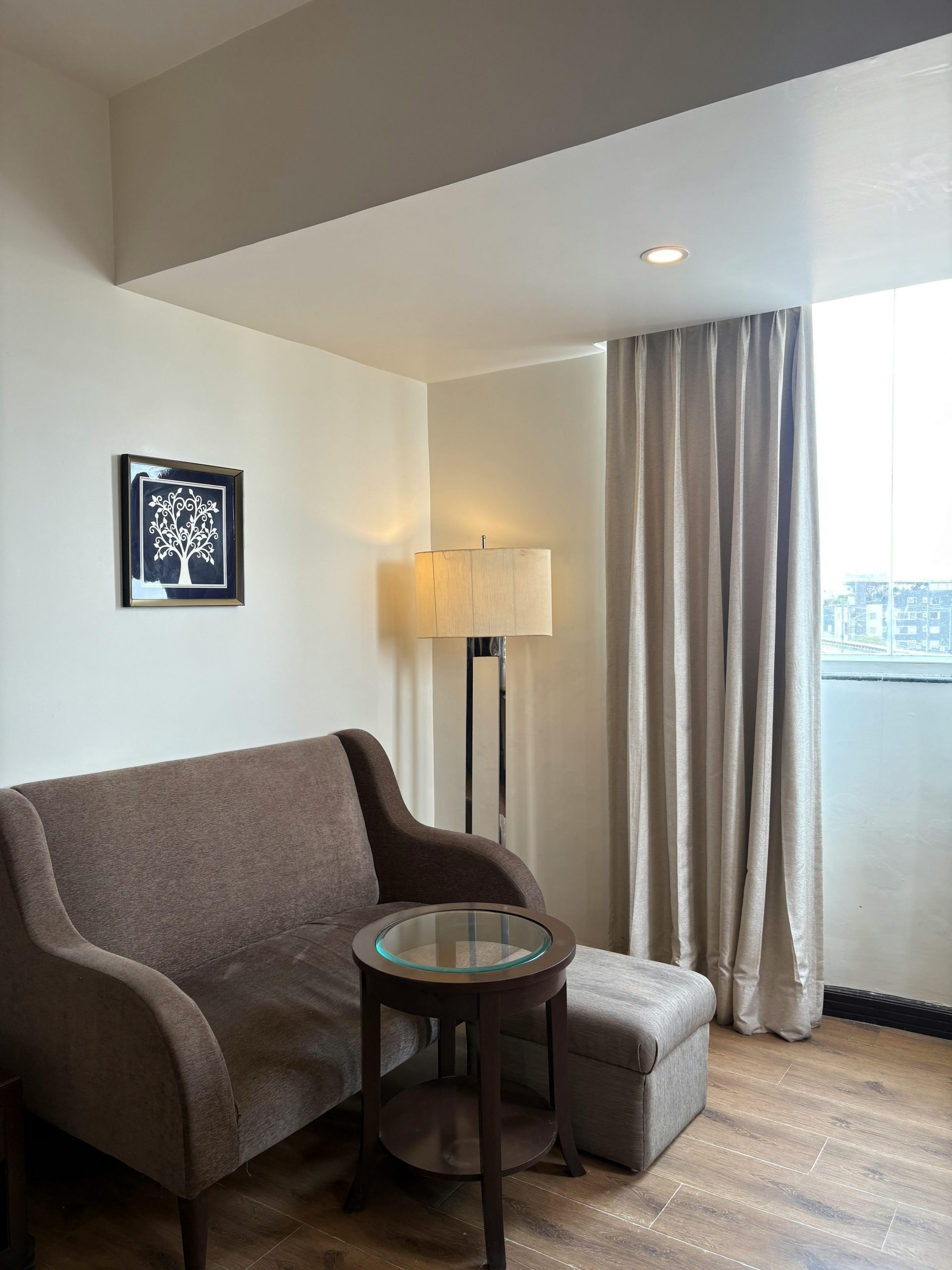 A cozy living room featuring a sofa, lamp, and artwork, with natural light.