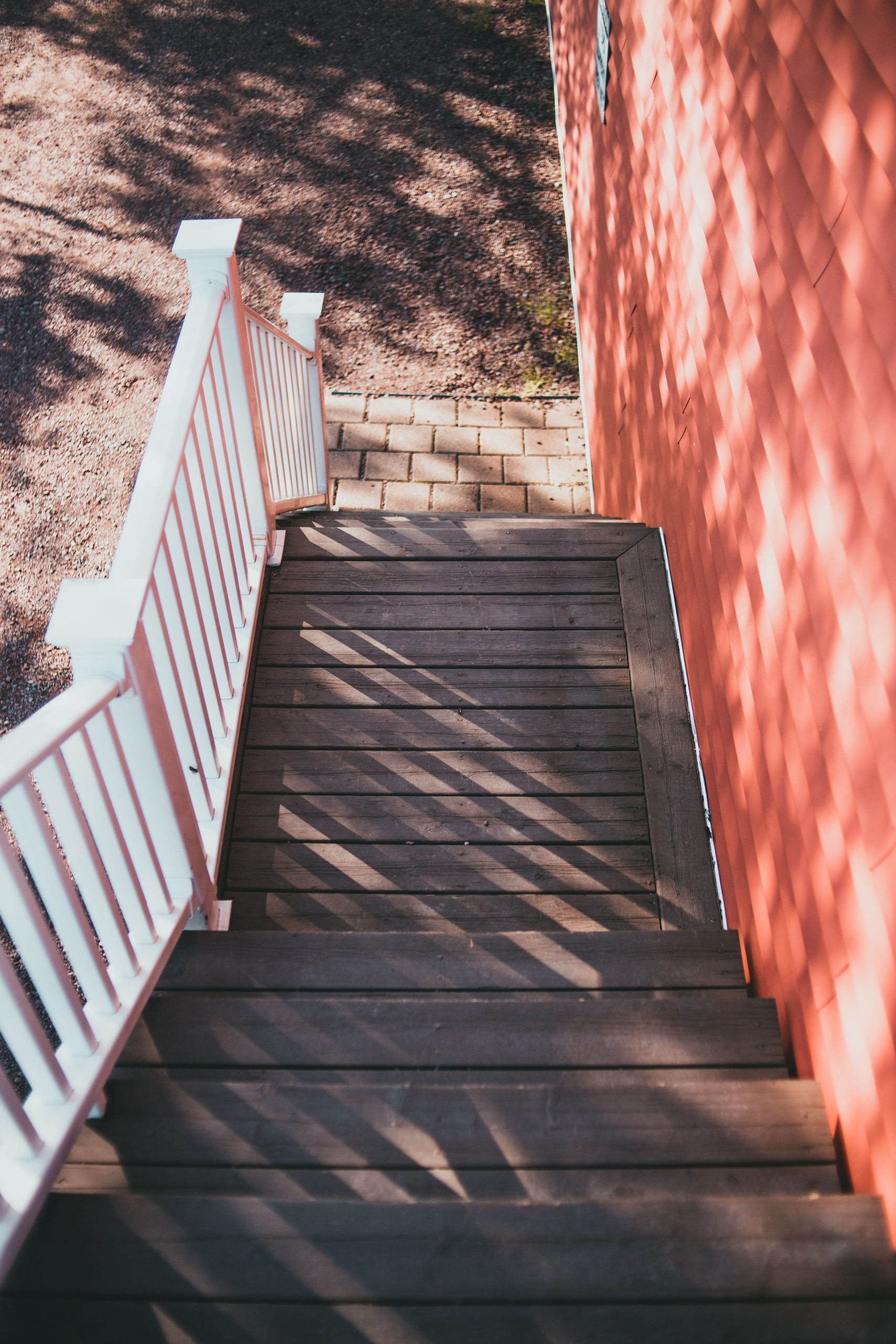 A cozy wooden staircase with sunlight casting intricate shadows, alongside a red wall.
