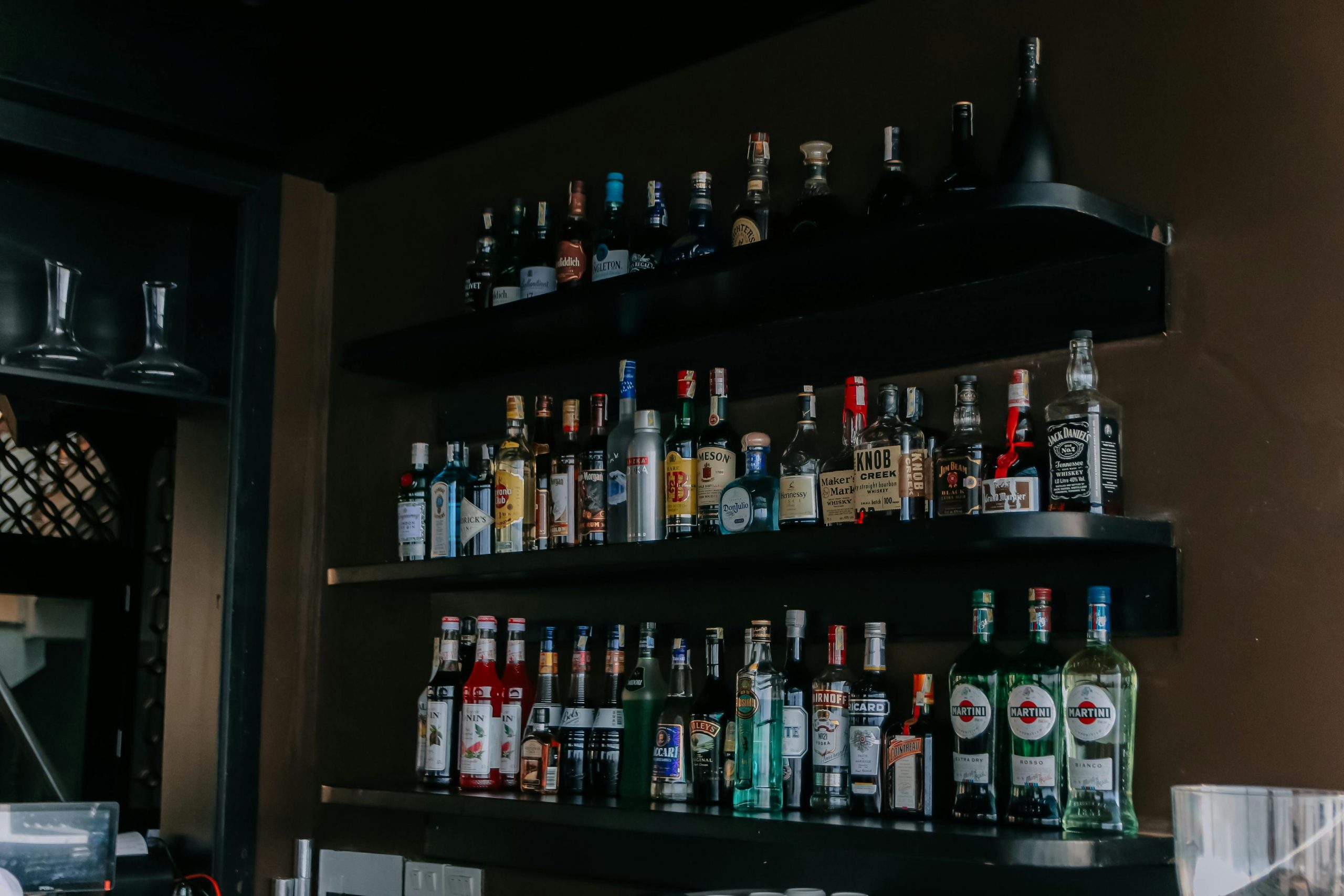 A modern bar with a wide selection of liquor bottles arranged on sleek black shelves.