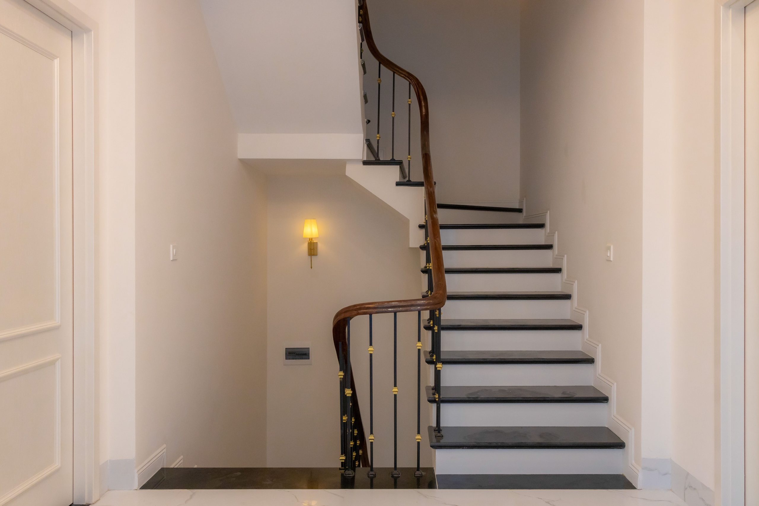 A modern, elegant staircase featuring a wooden handrail and light wall sconce in an indoor setting.