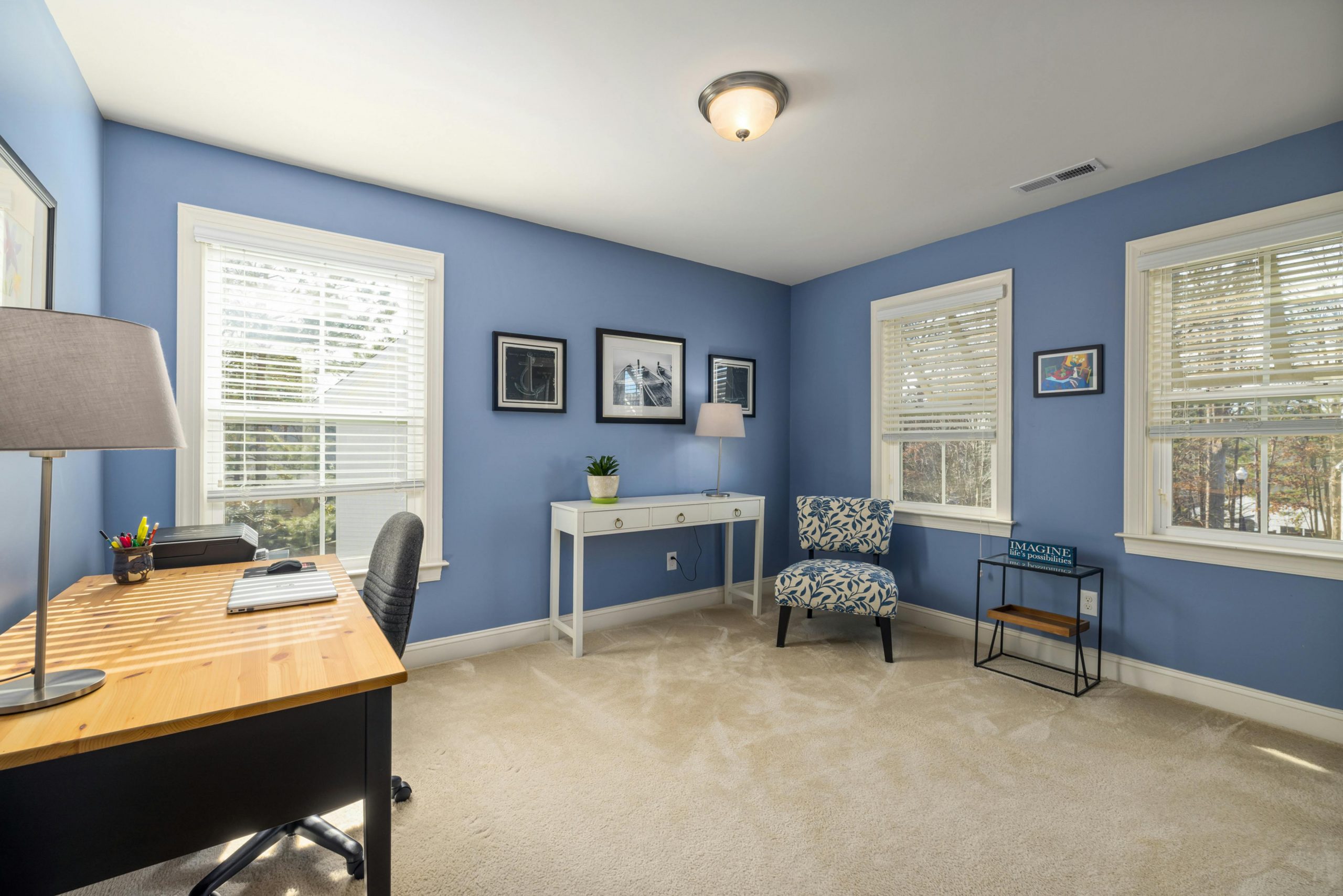 A modern home office with blue walls and natural light from windows.