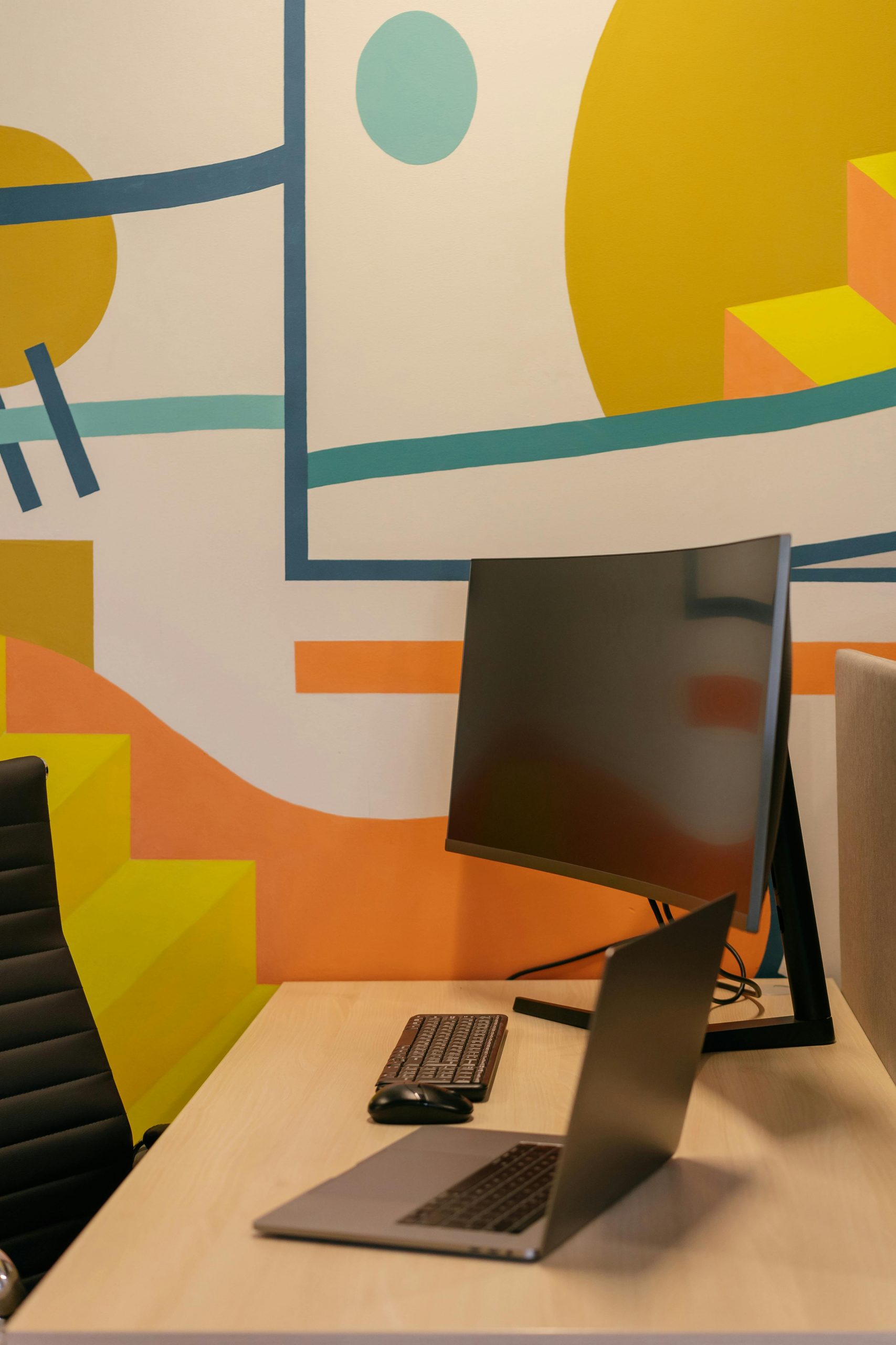 A modern office desk with a laptop, monitor, and vibrant abstract wall art for a creative workspace.