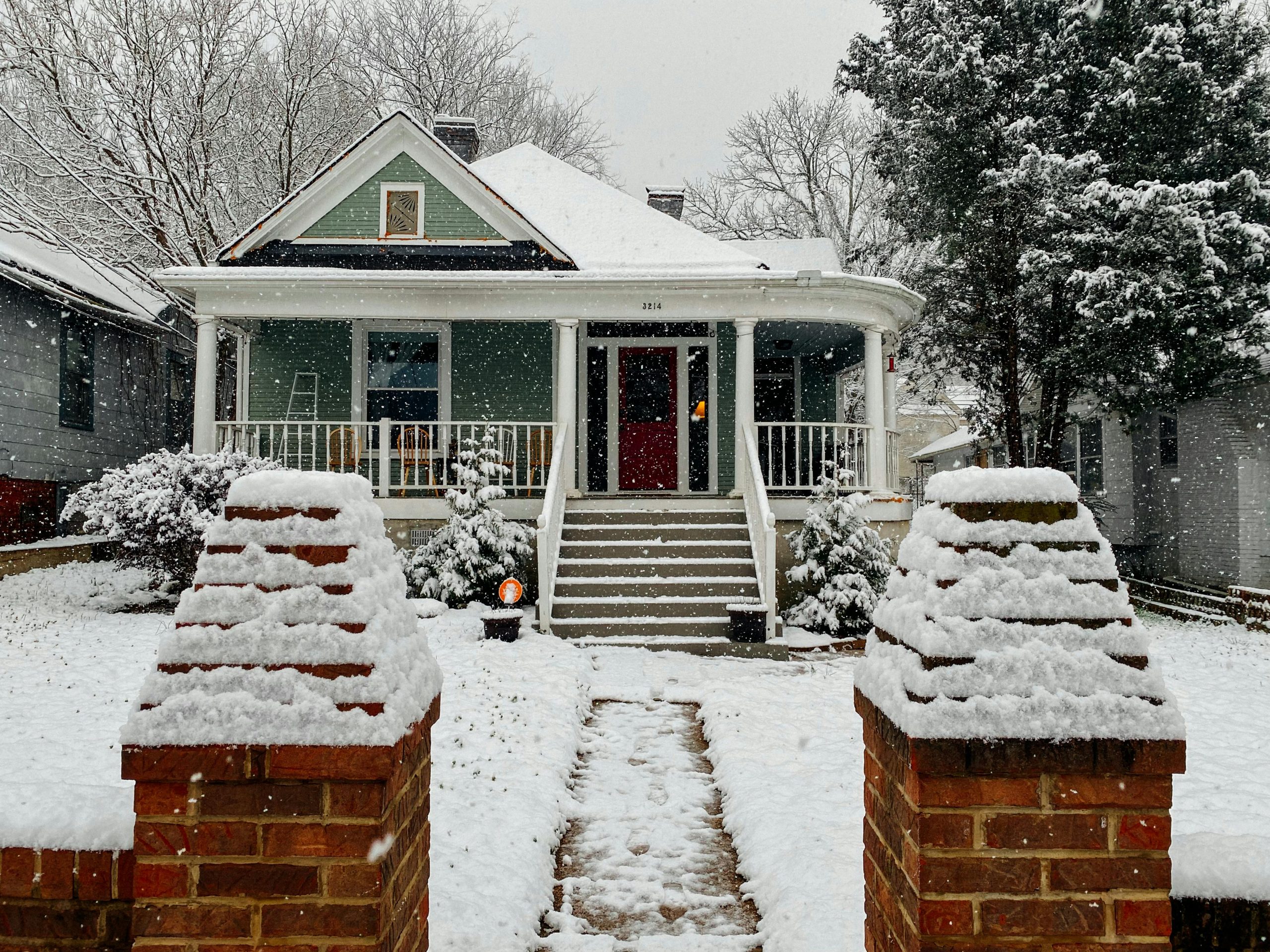 A picturesque bungalow with a snow-covered roof and trees depicting a serene winter scene.