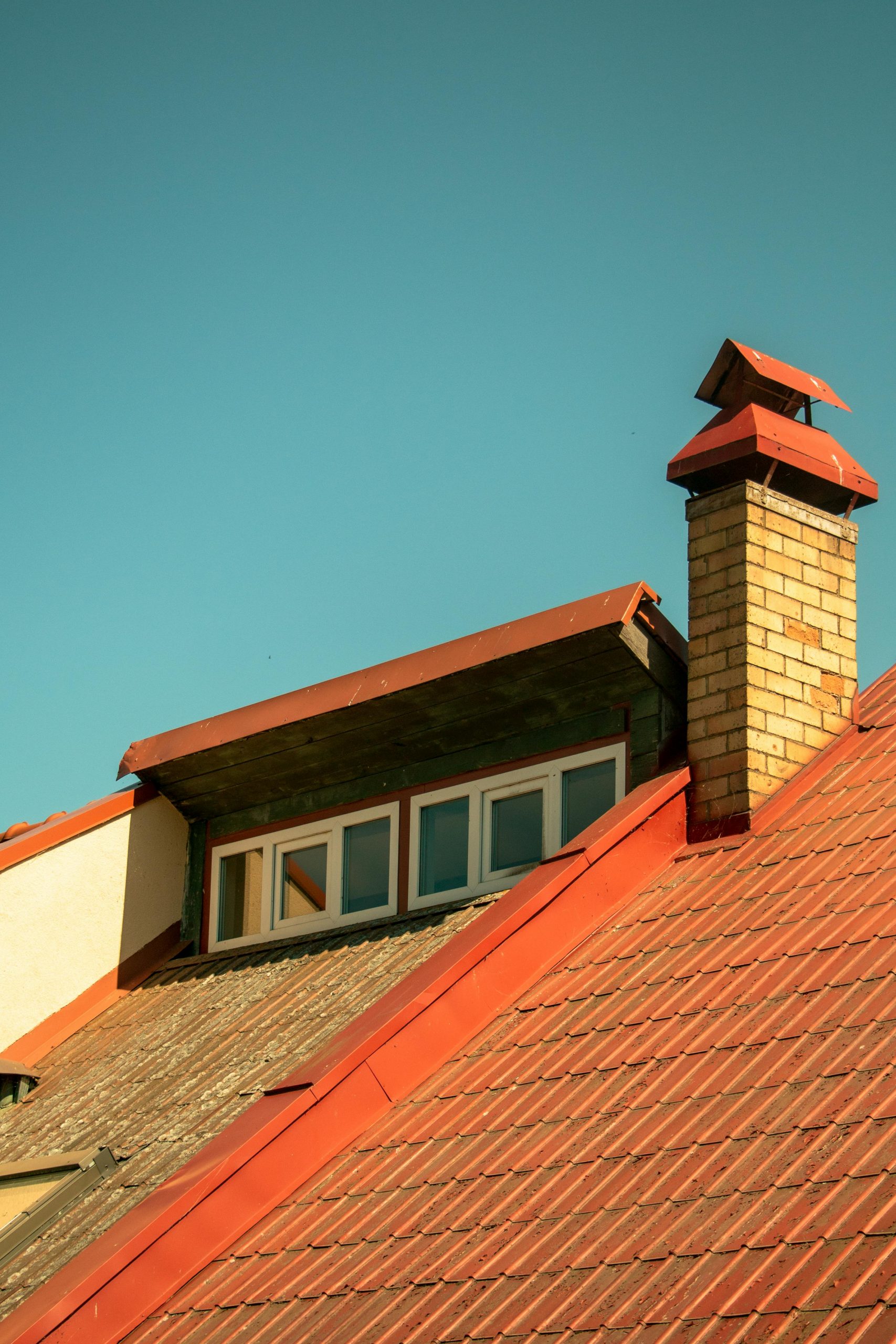 A rooftop featuring a sunlit brick chimney and skylight under a clear blue sky.