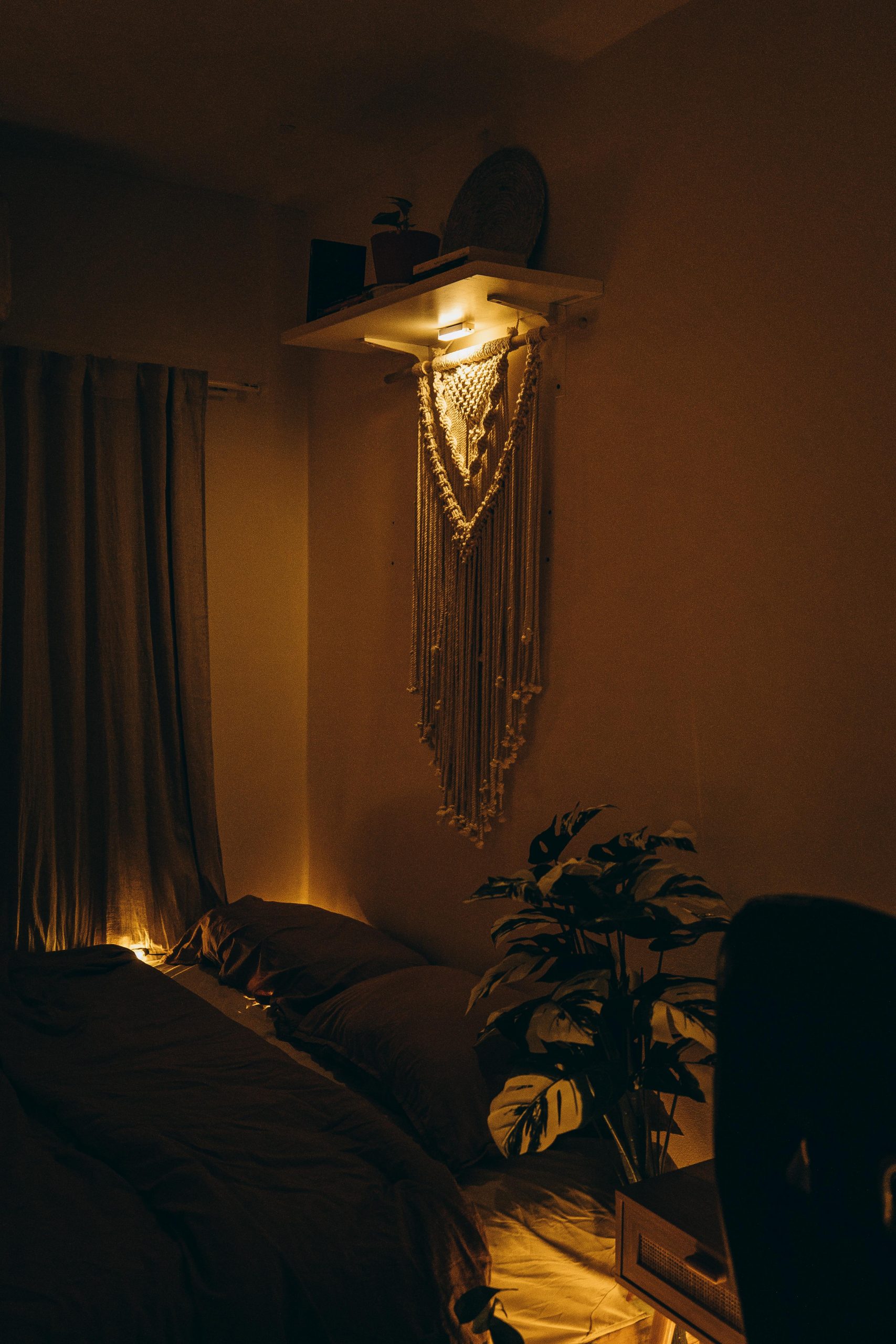 A serene bedroom featuring warm ambient lighting, macrame wall decor, and lush plant accents.