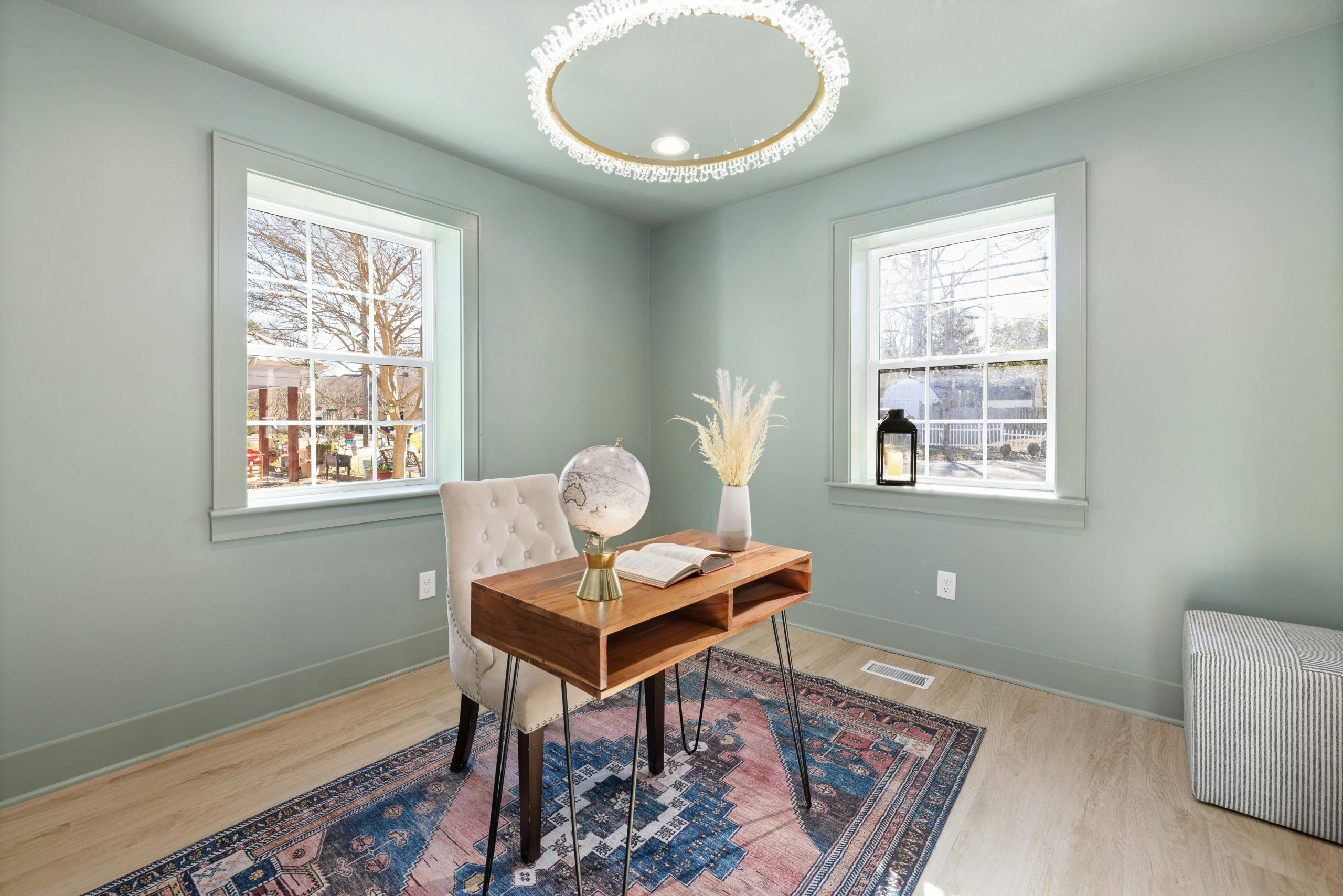 A serene home office with chic decor, featuring a wooden desk, tufted chair, and large windows for natural light.