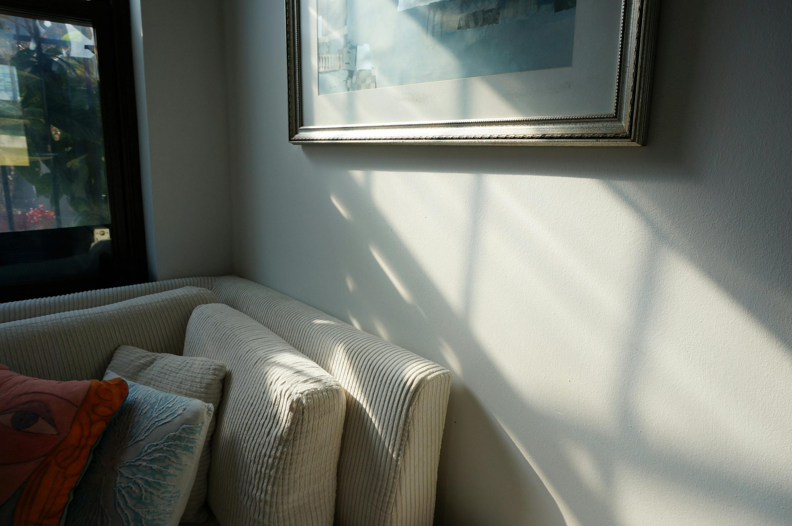 A serene living room corner with a couch and pillows, bathed in soft sunlight.