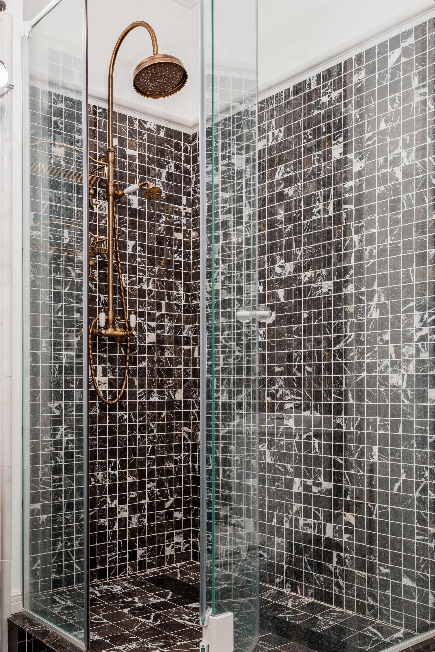 A stylish modern shower with bronze fixtures and mosaic tiled walls in a cabin-style bathroom.