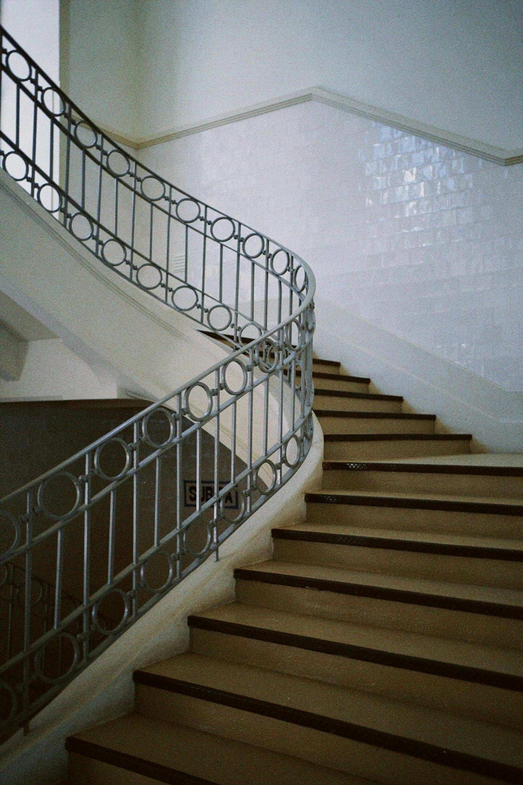 An elegant indoor staircase with a curved metal railing and white walls.