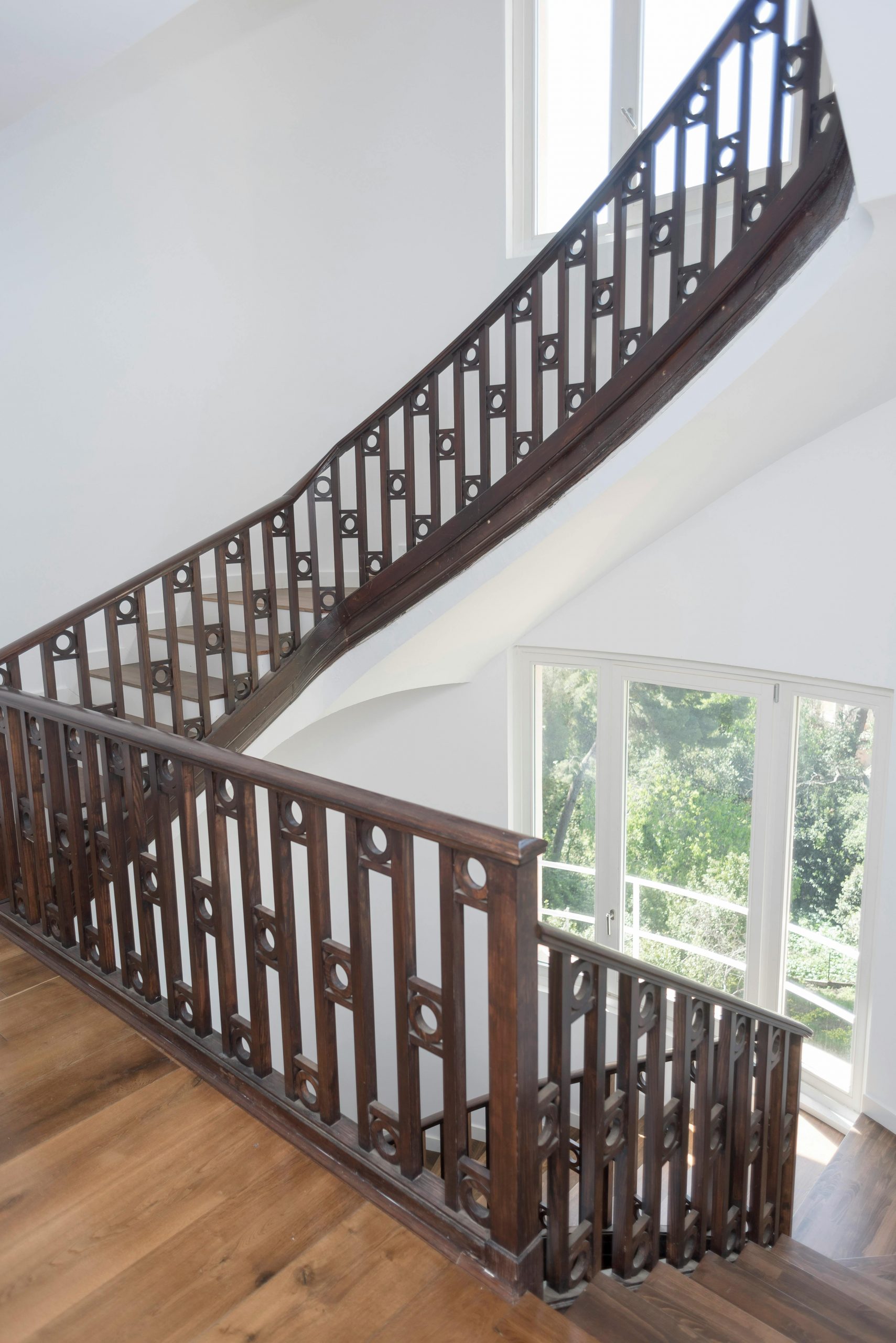 Beautiful wooden staircase with intricate railing in a sunlit interior space.