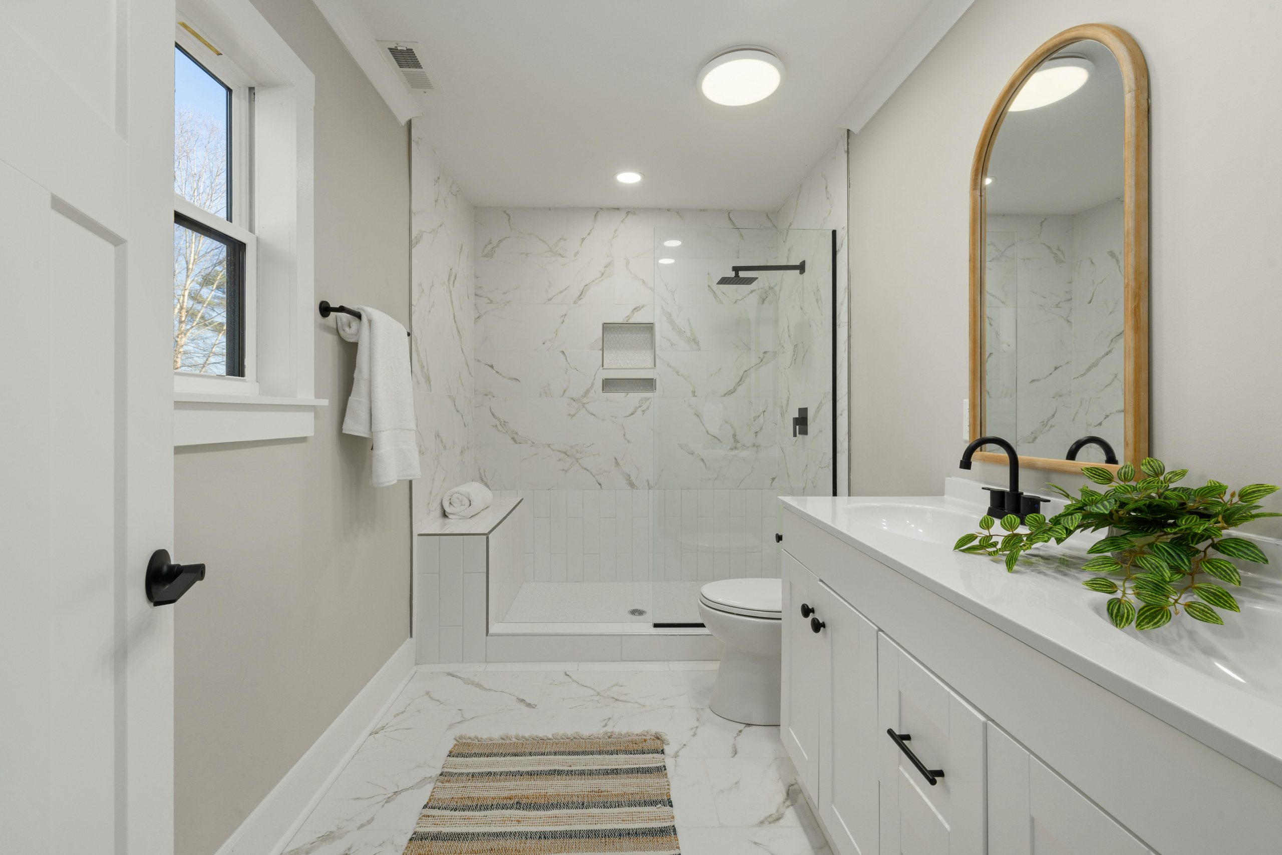 Bright modern bathroom featuring marble shower, large mirror, and sleek faucets.