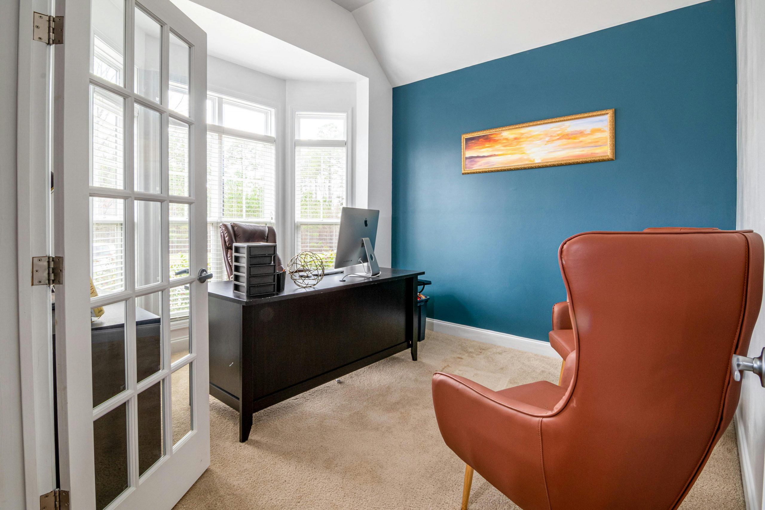 Bright office room with blue accent wall, featuring leather chair and desk in natural light.