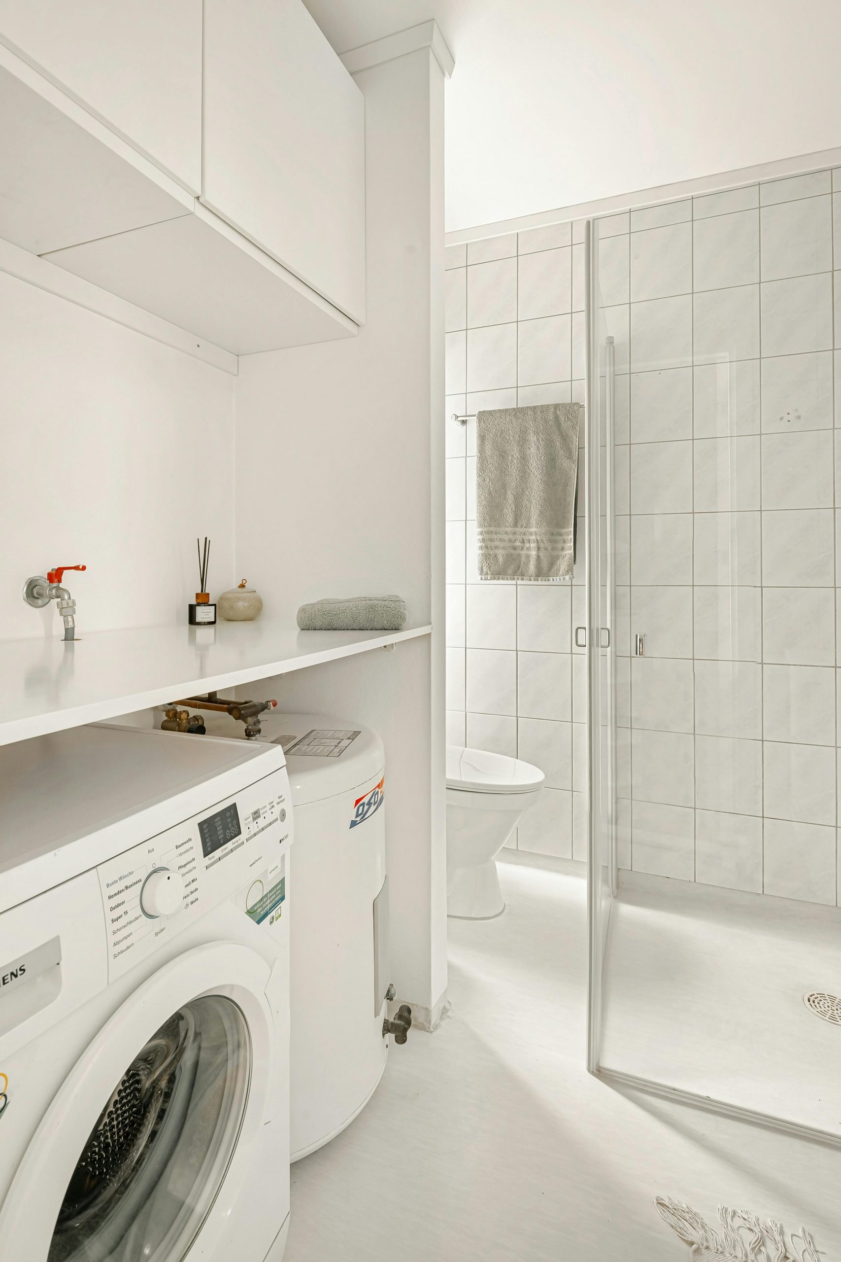 Bright white bathroom with integrated laundry area featuring a washing machine and shower.