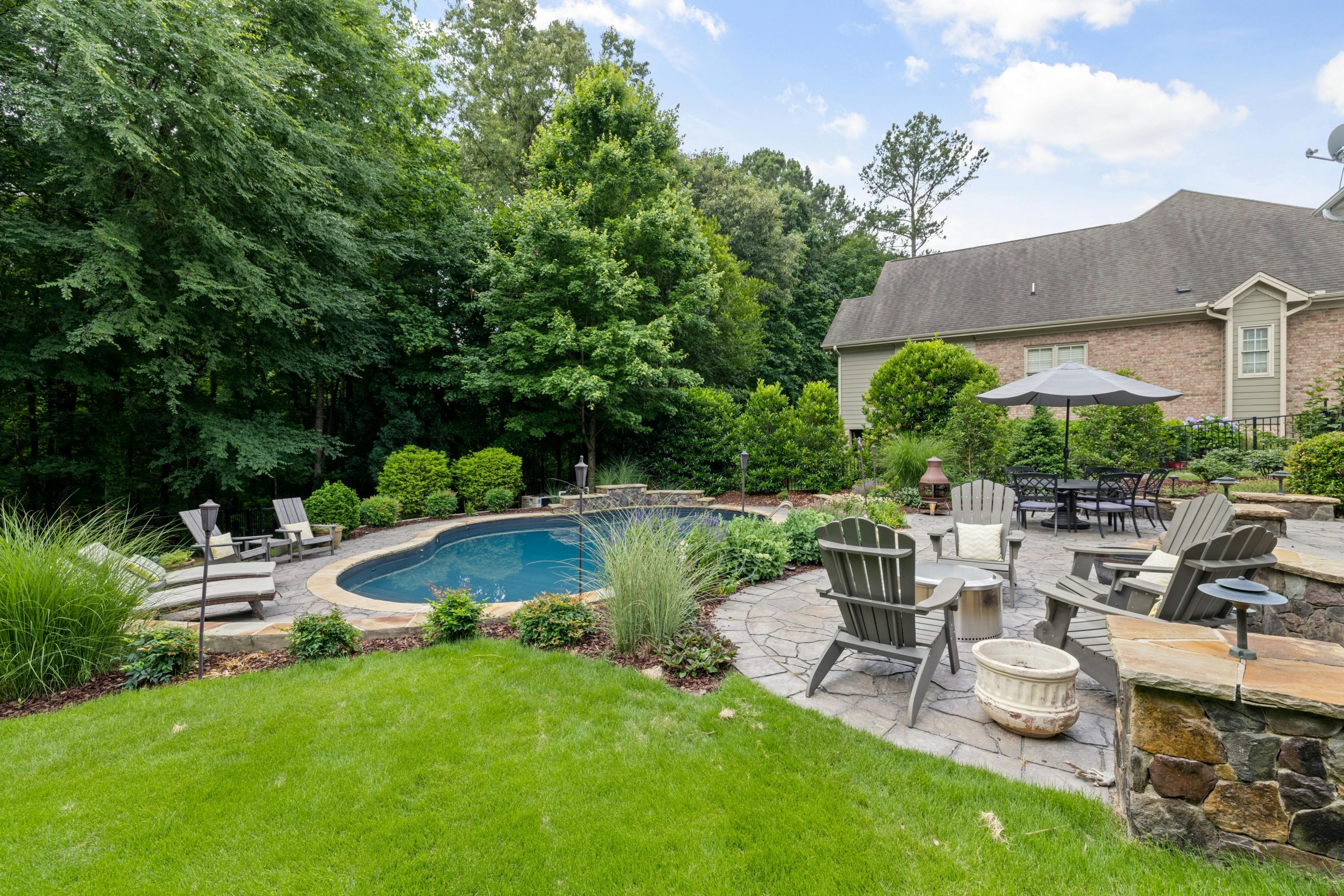 Charming backyard featuring a pool, patio with furniture, and lush greenery.