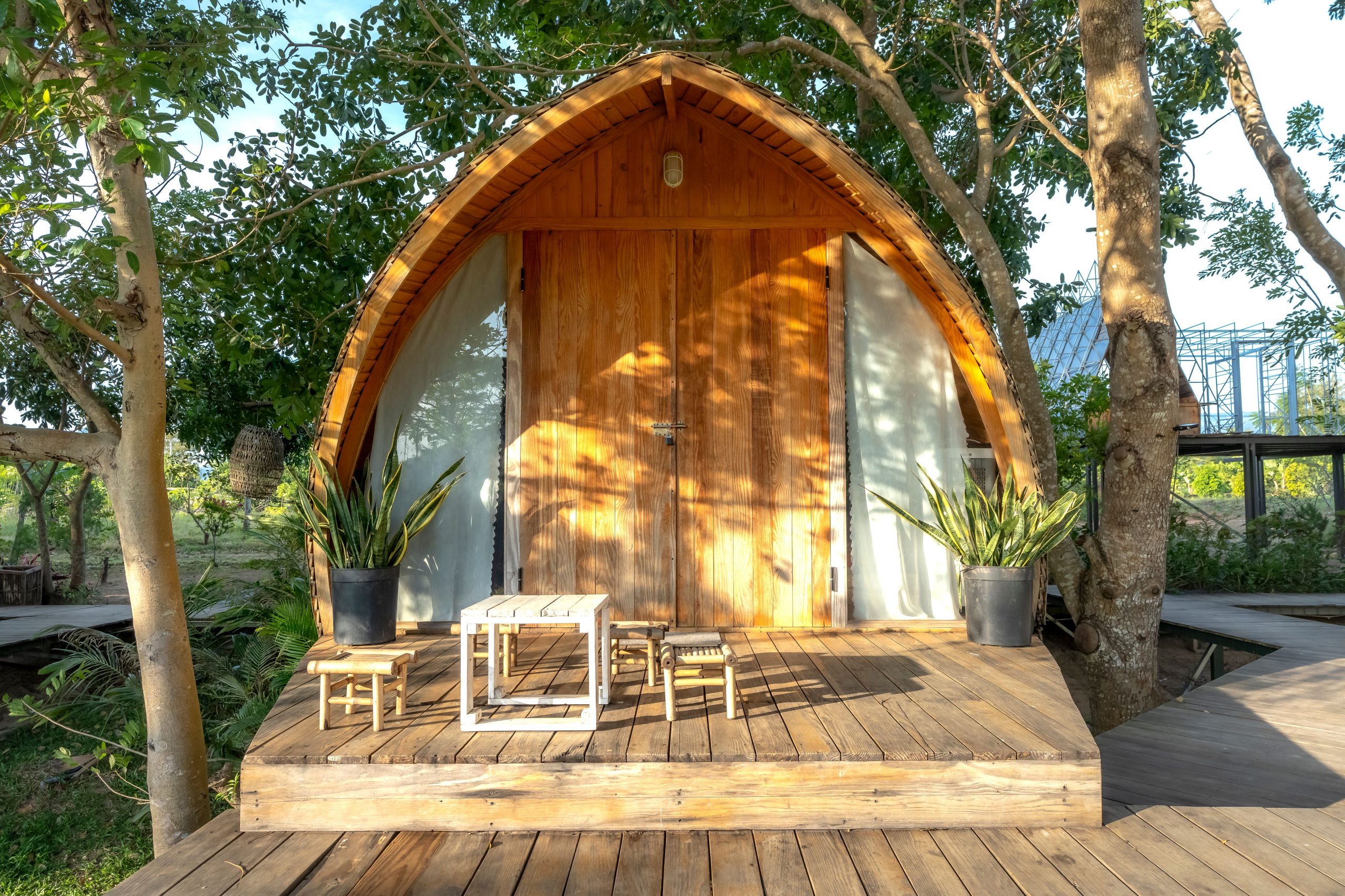Charming wooden cabin with a small patio, nestled in lush greenery, under bright daylight, ideal for nature retreats.
