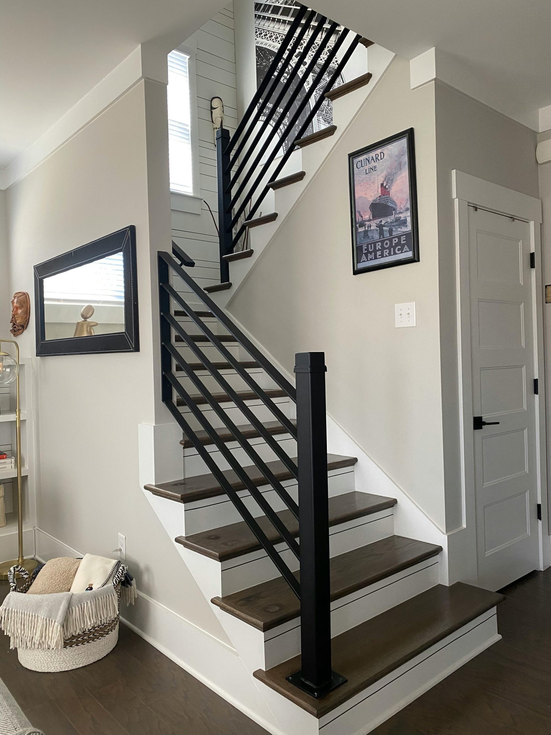Contemporary interior featuring a staircase with black railings, a mirror, and framed art.