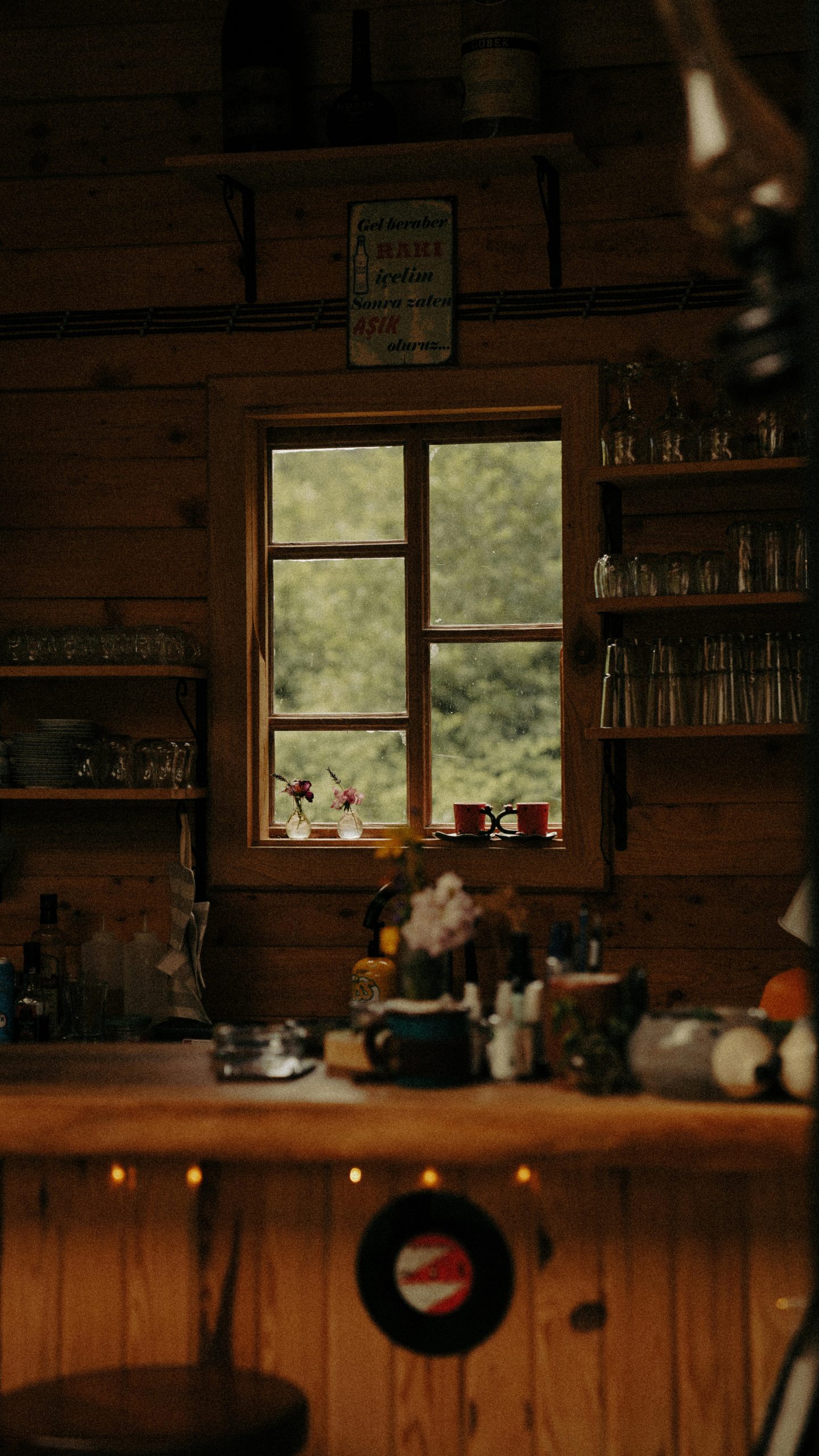 Cozy bar interior with wooden accents, glassware, and a scenic window view of lush greenery.