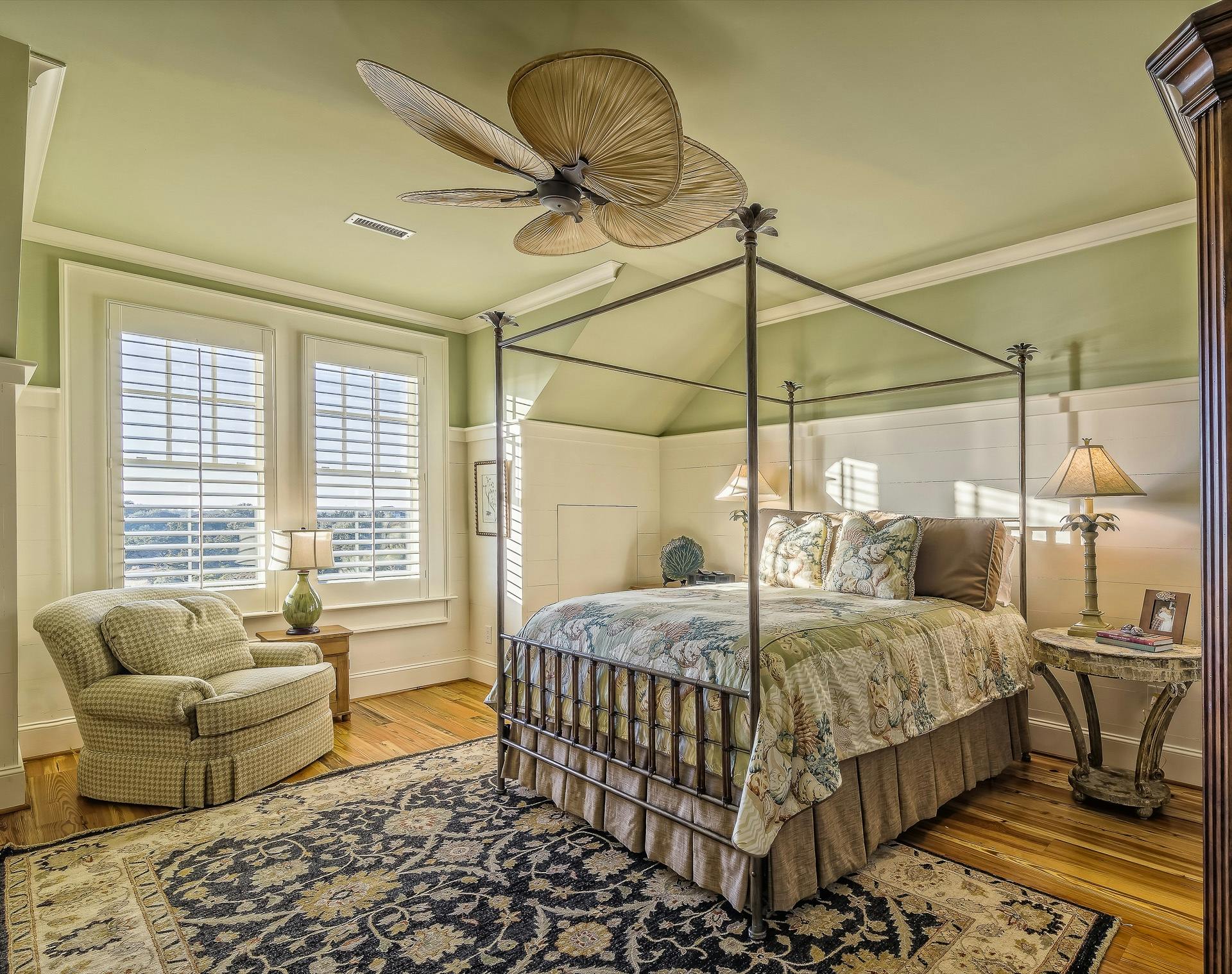Cozy bedroom featuring a four-poster bed, ornate rug, and natural light from shuttered windows.