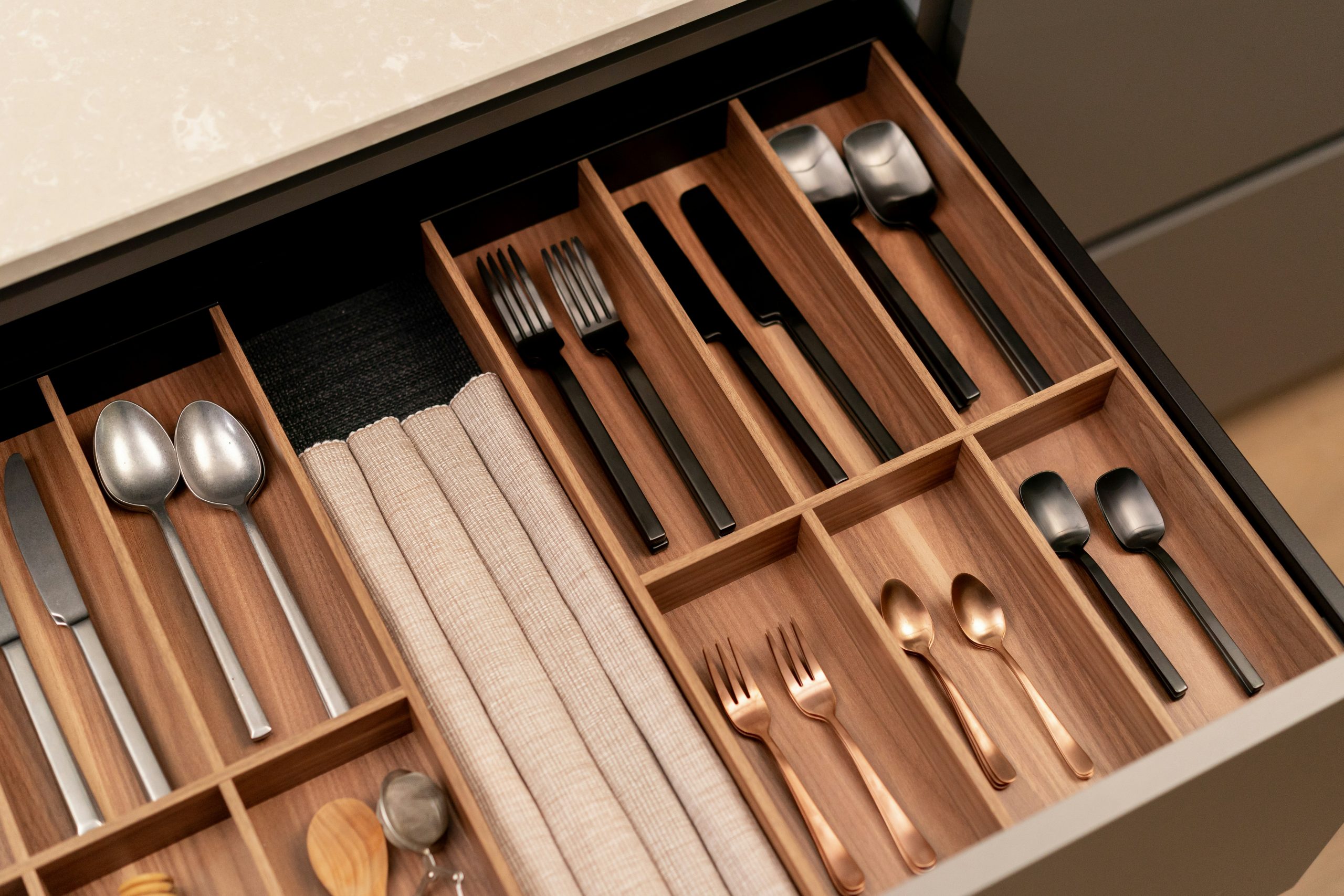 Cutlery drawer with black, gold and silver cutlery and cooking untensils with wooden details.