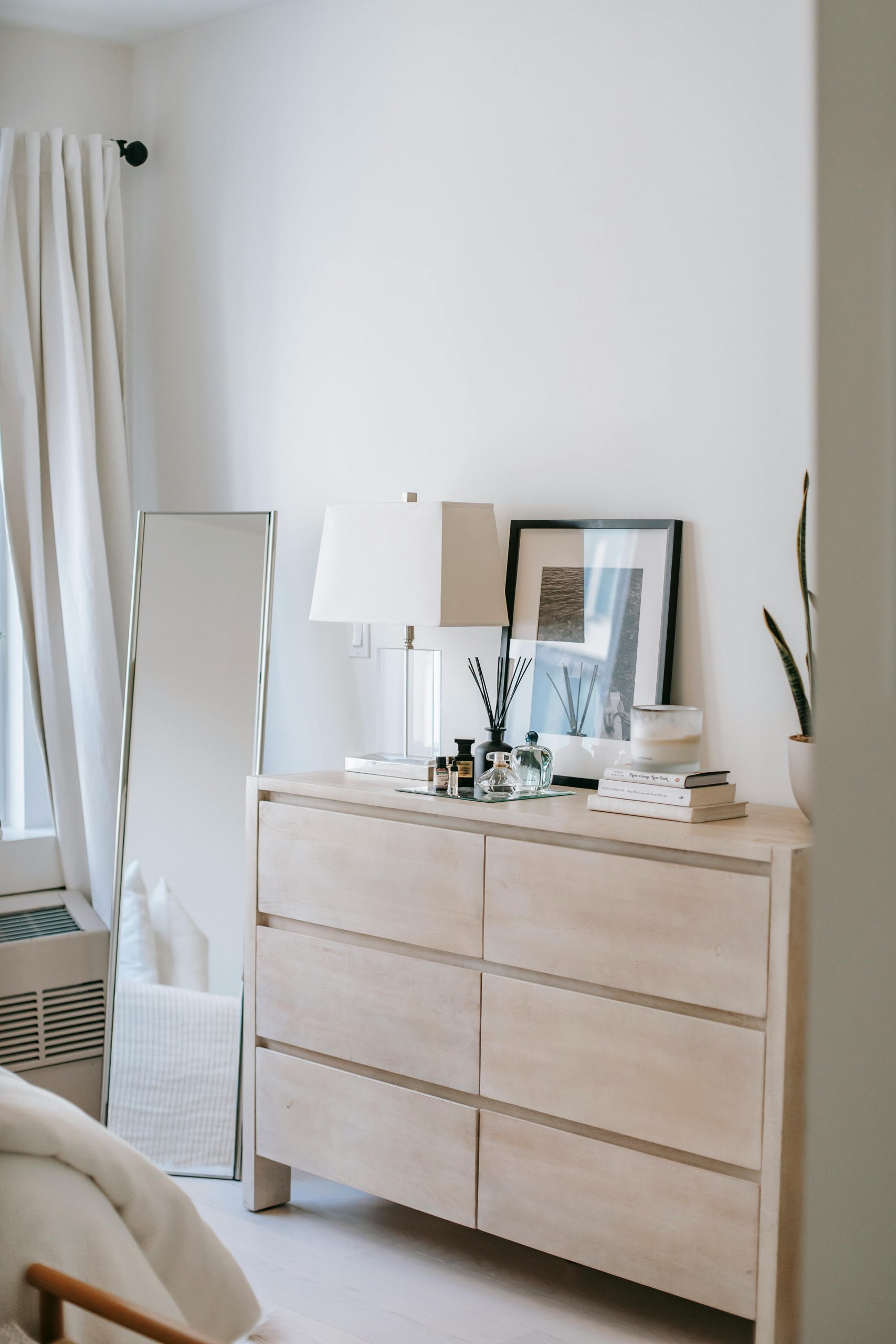 Decorative bottles and photo on wooden commode near rectangular shaped mirror on floor at home