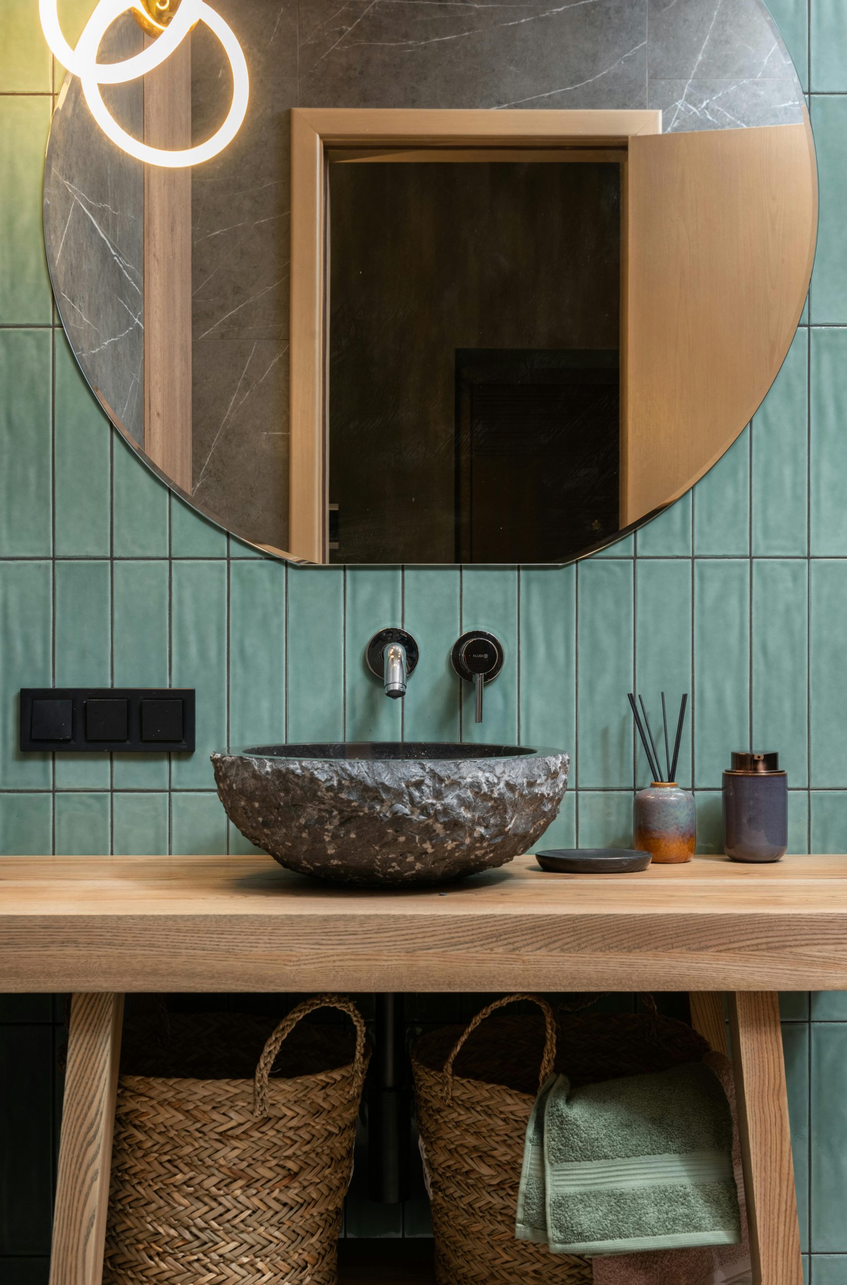 Elegant bathroom featuring stone basin, round mirror, and green tiles.