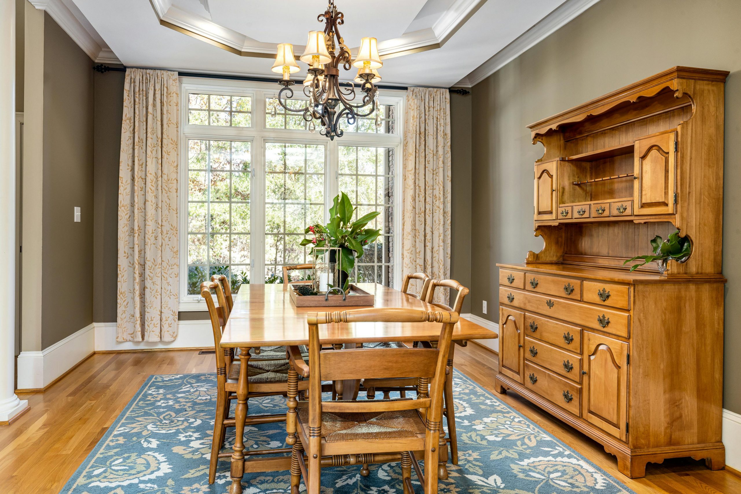 Elegant dining room with wooden furniture, chandelier, and natural light from large windows.